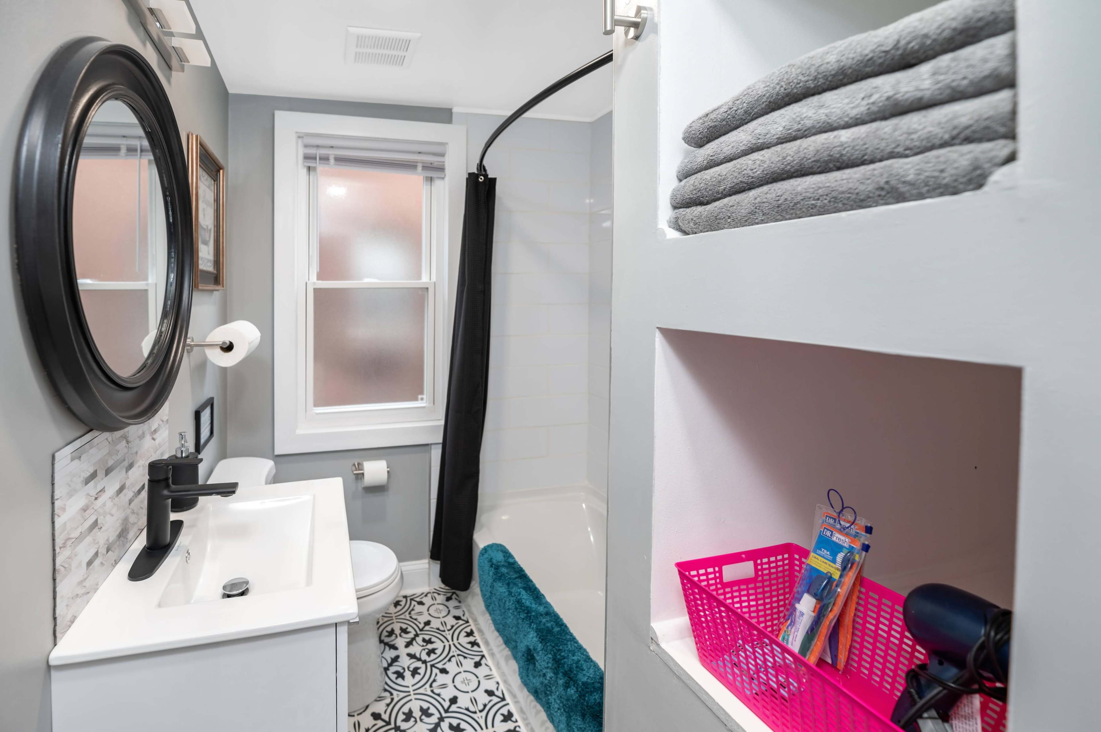 A bathroom featuring a shower, a sink with a mirror, a toilet, and neatly stacked towels on a shelf.