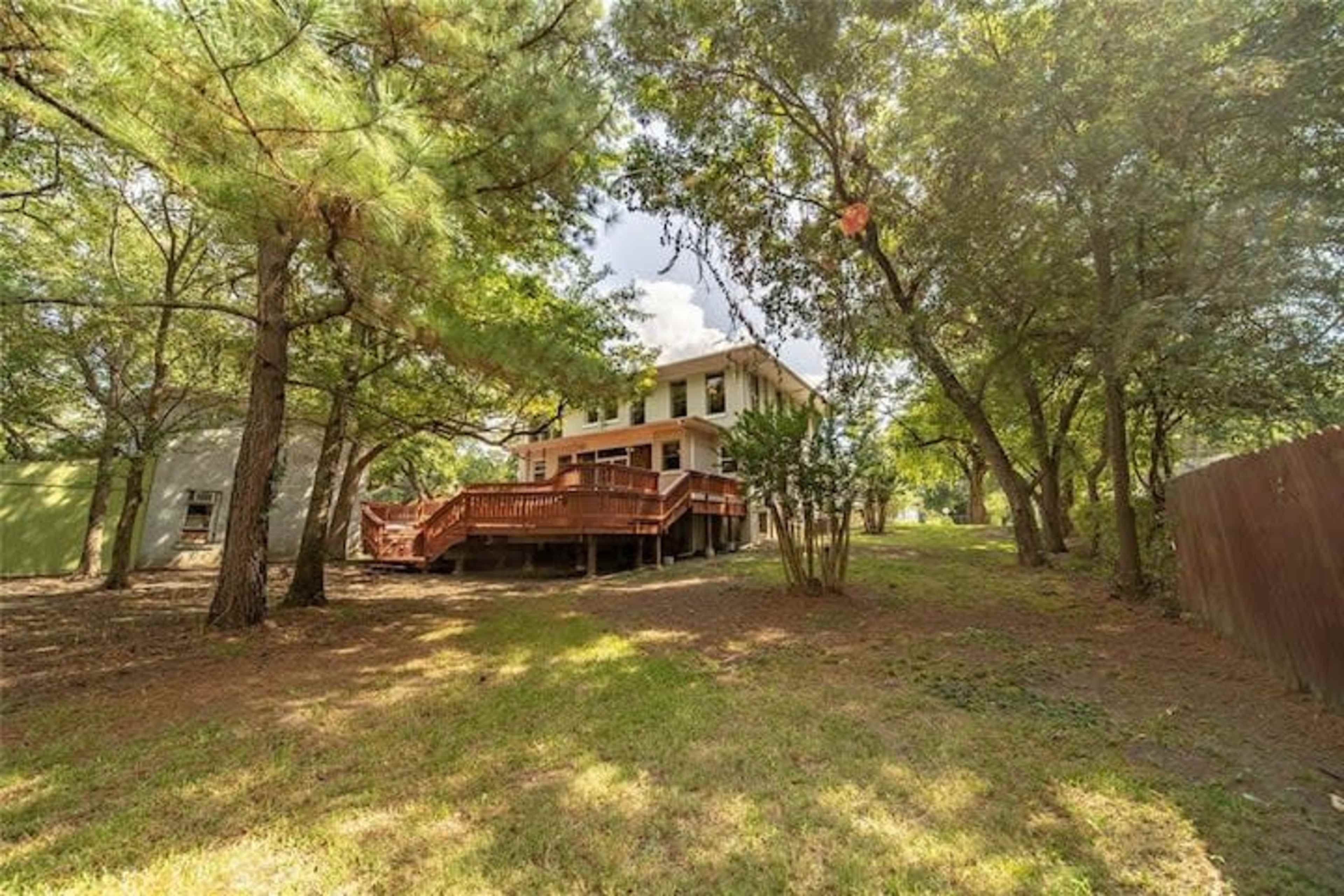 A two-story house with a wooden deck is surrounded by trees in a residential area.