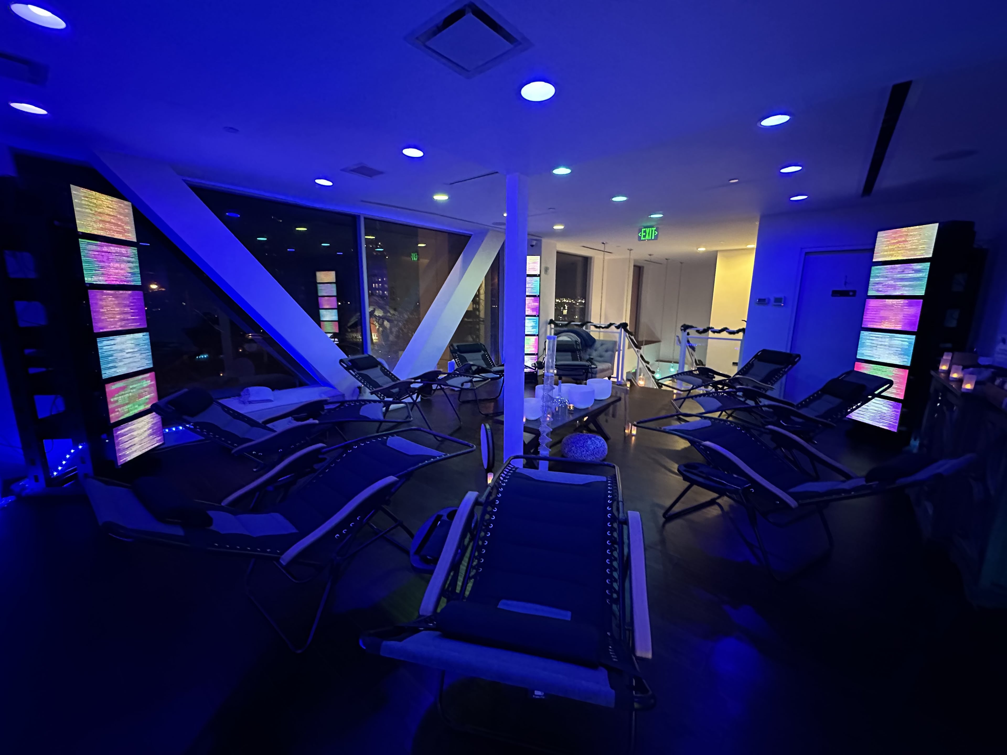 The image shows a dimly lit relaxation room with several loungers arranged around illuminated vertical screens, creating a serene atmosphere.