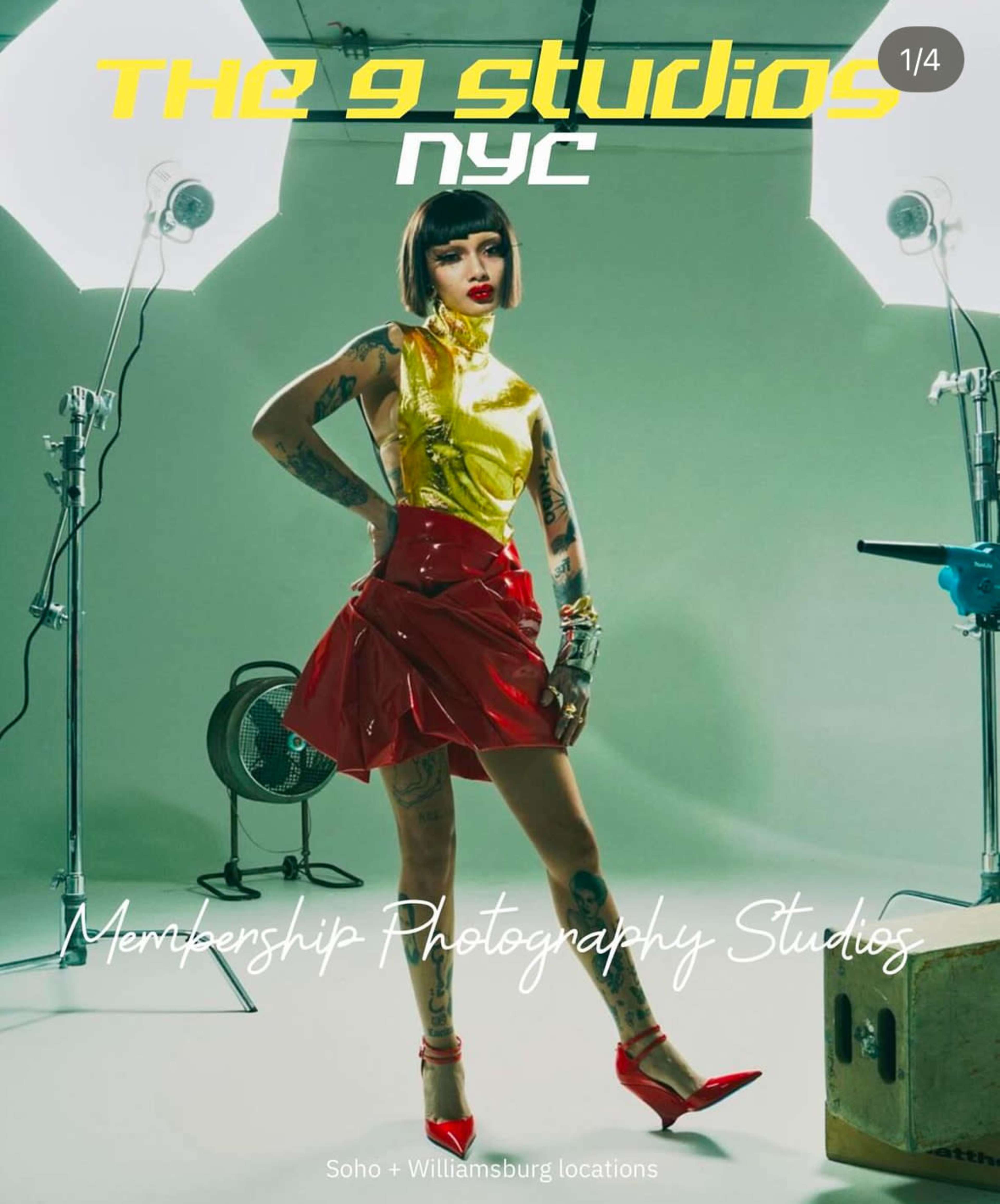 A model stands confidently in a studio, wearing a bright yellow top and red skirt, with professional lighting equipment positioned around her.