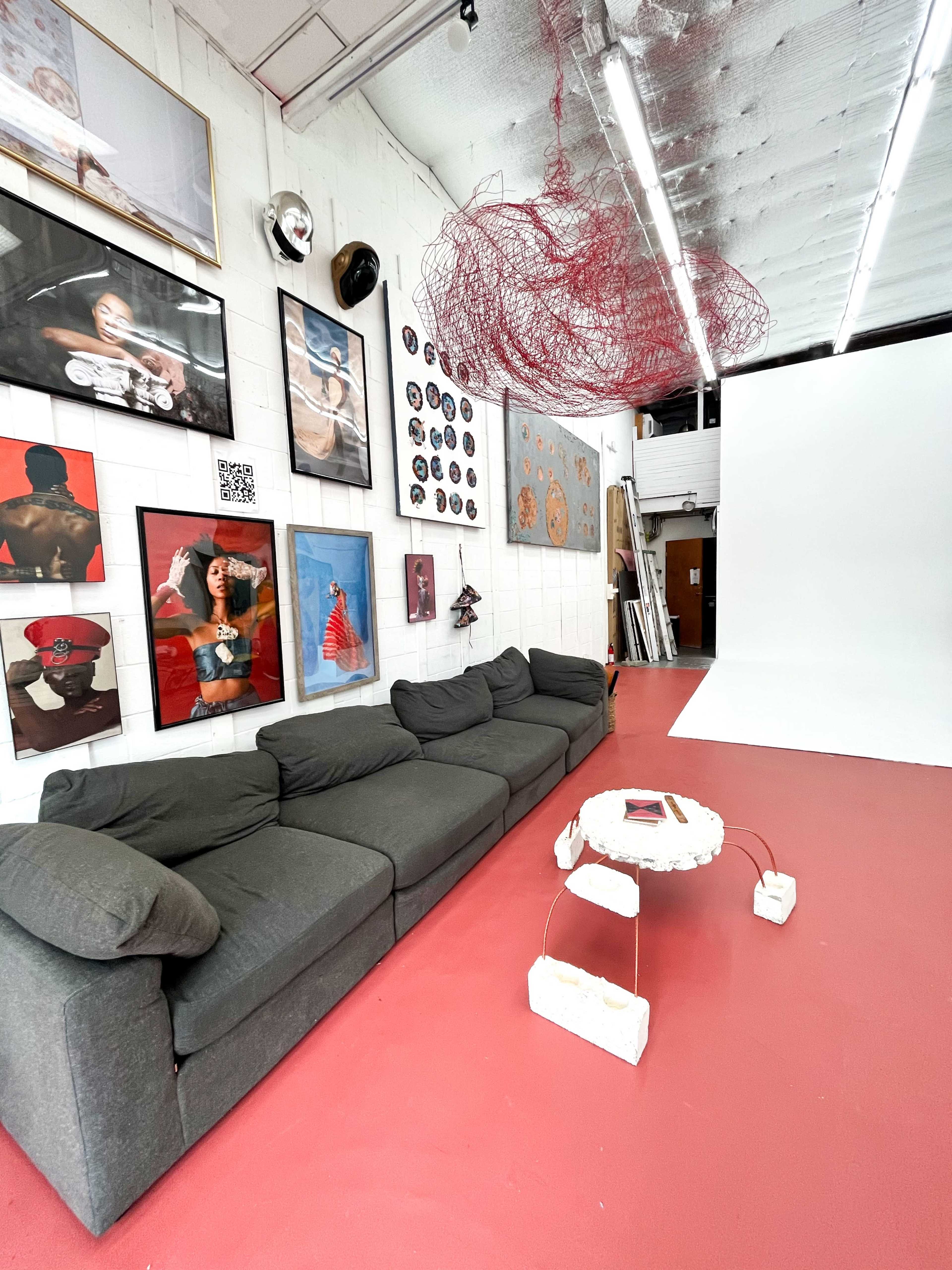 A spacious studio with a gray couch, a collection of framed artwork on the walls, and a white backdrop set up for photography.