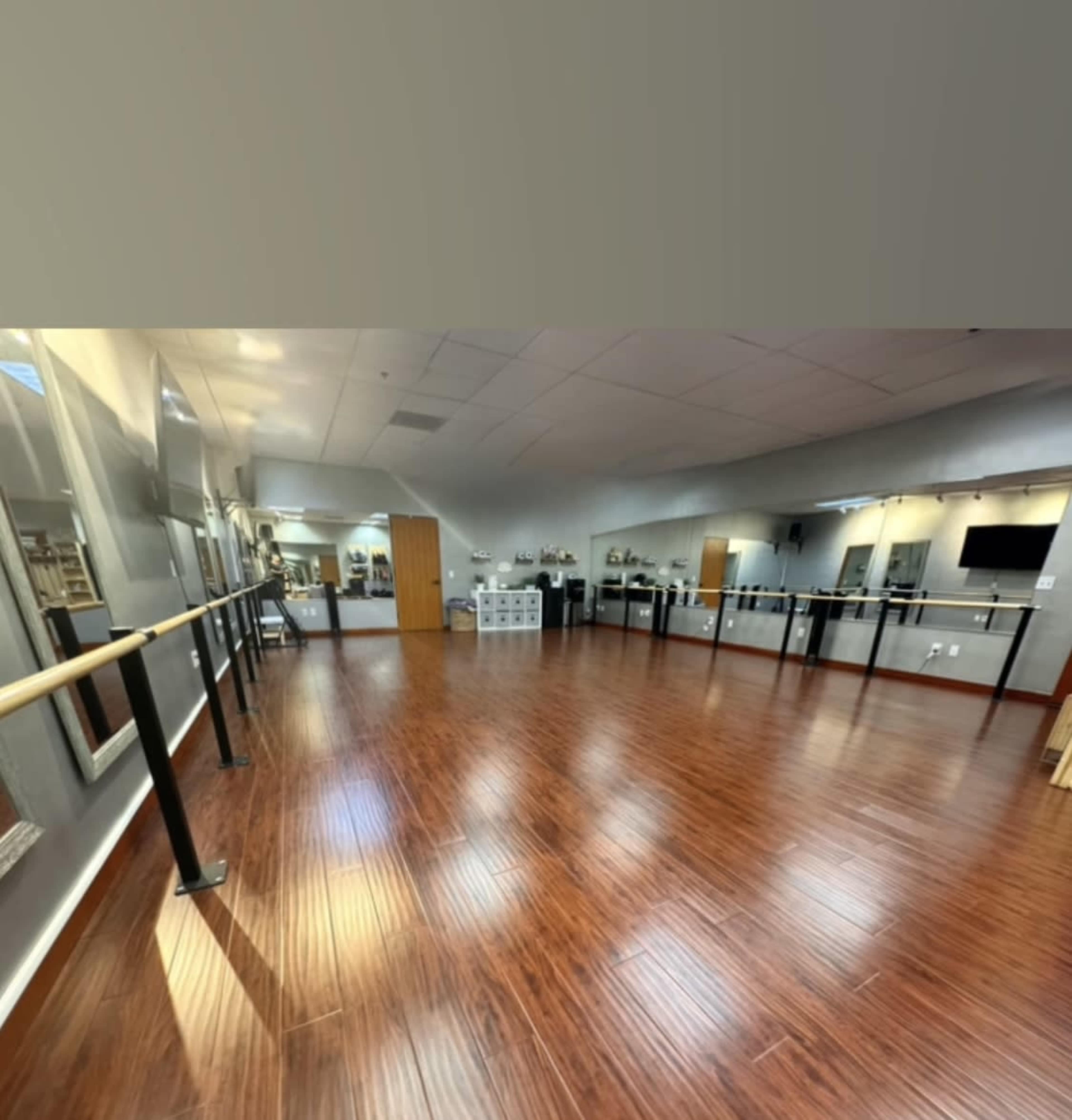 The image shows an empty dance studio with wooden flooring, mirrored walls, and a ballet barre along one side.
