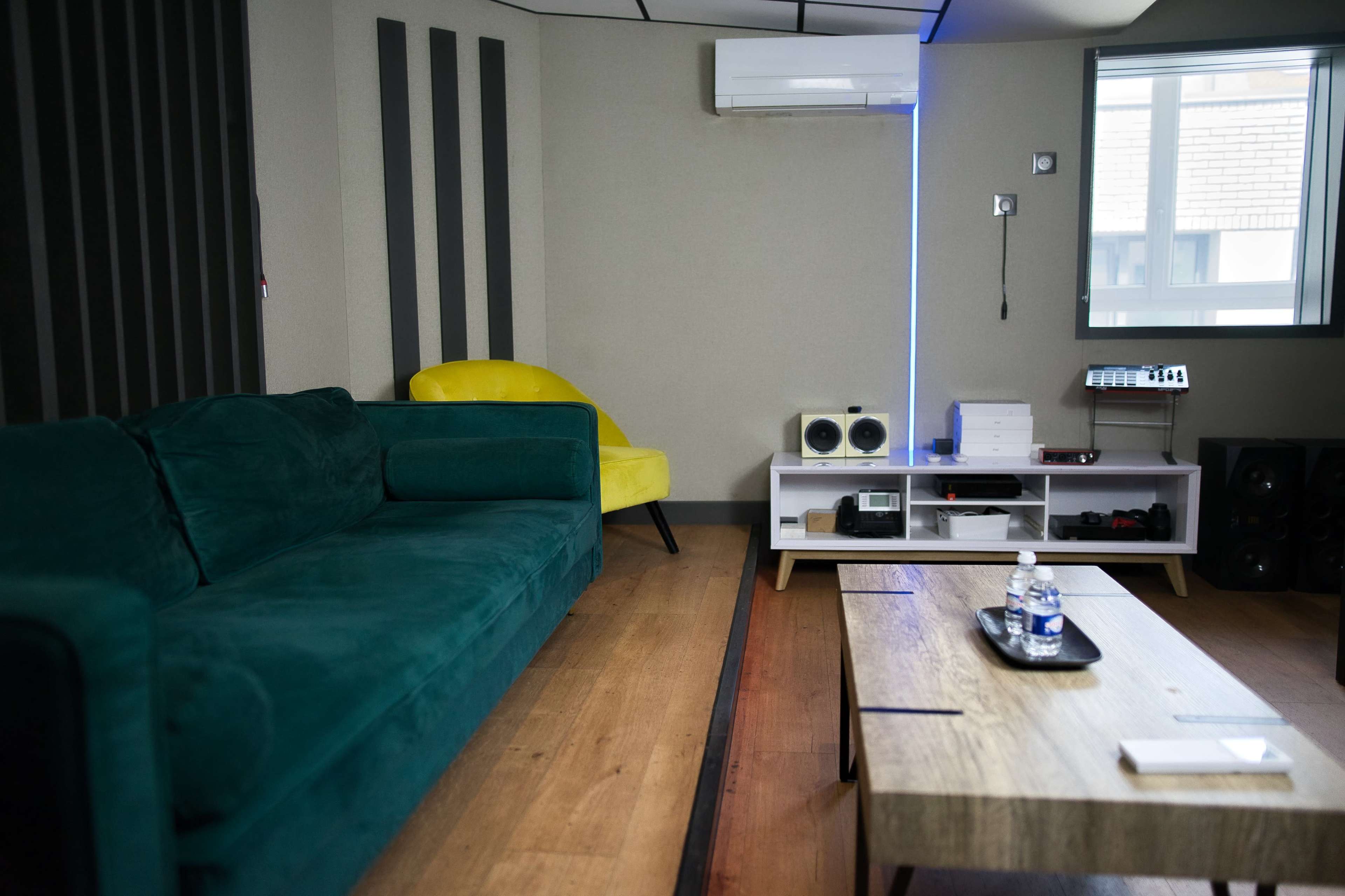 A modern room featuring a green couch, a yellow chair, a wooden coffee table, and various audio equipment against a neutral wall.