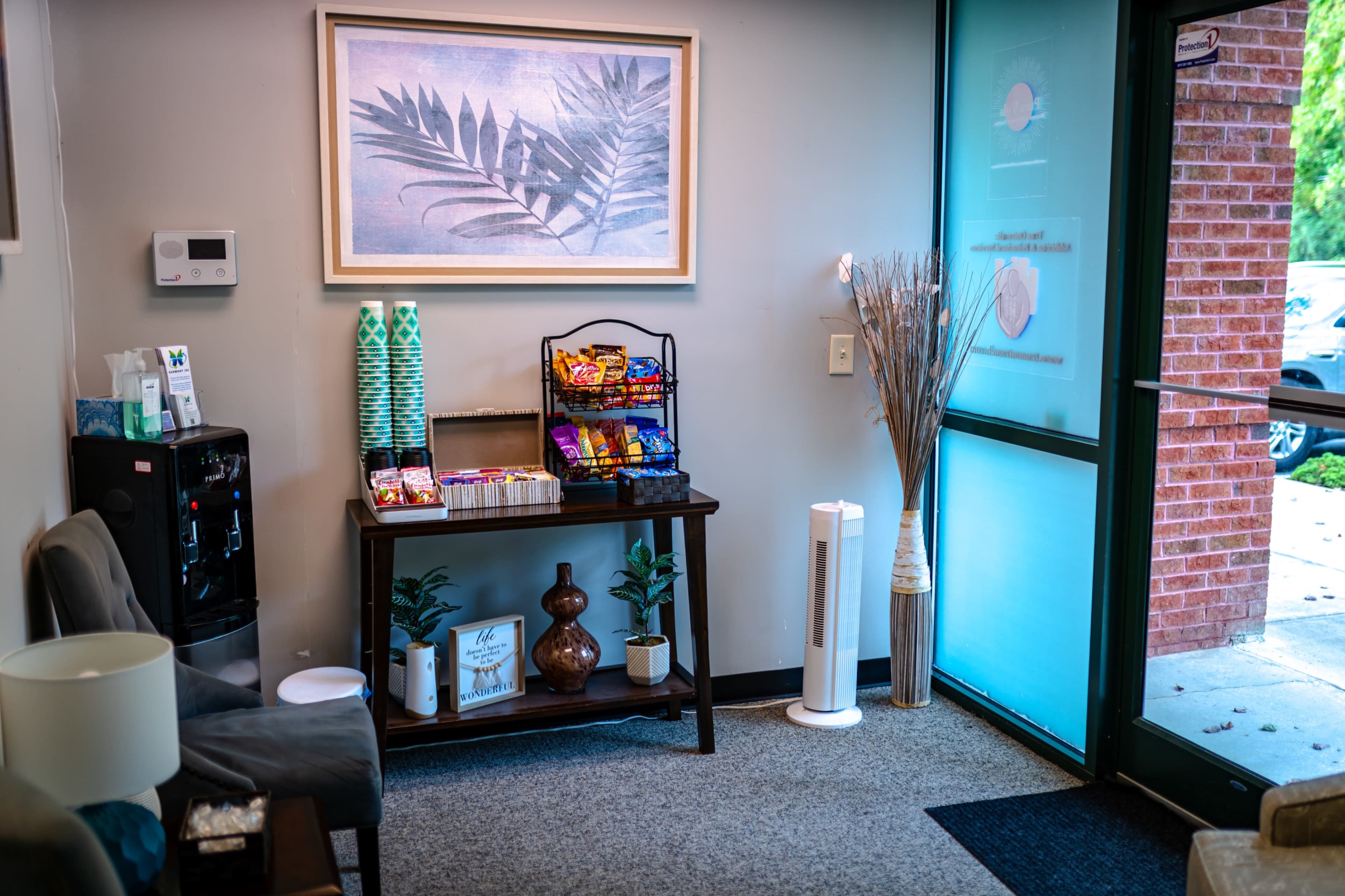 A reception area with a table displaying snacks, a water cooler, and seating, alongside a large window with a view of the outside.