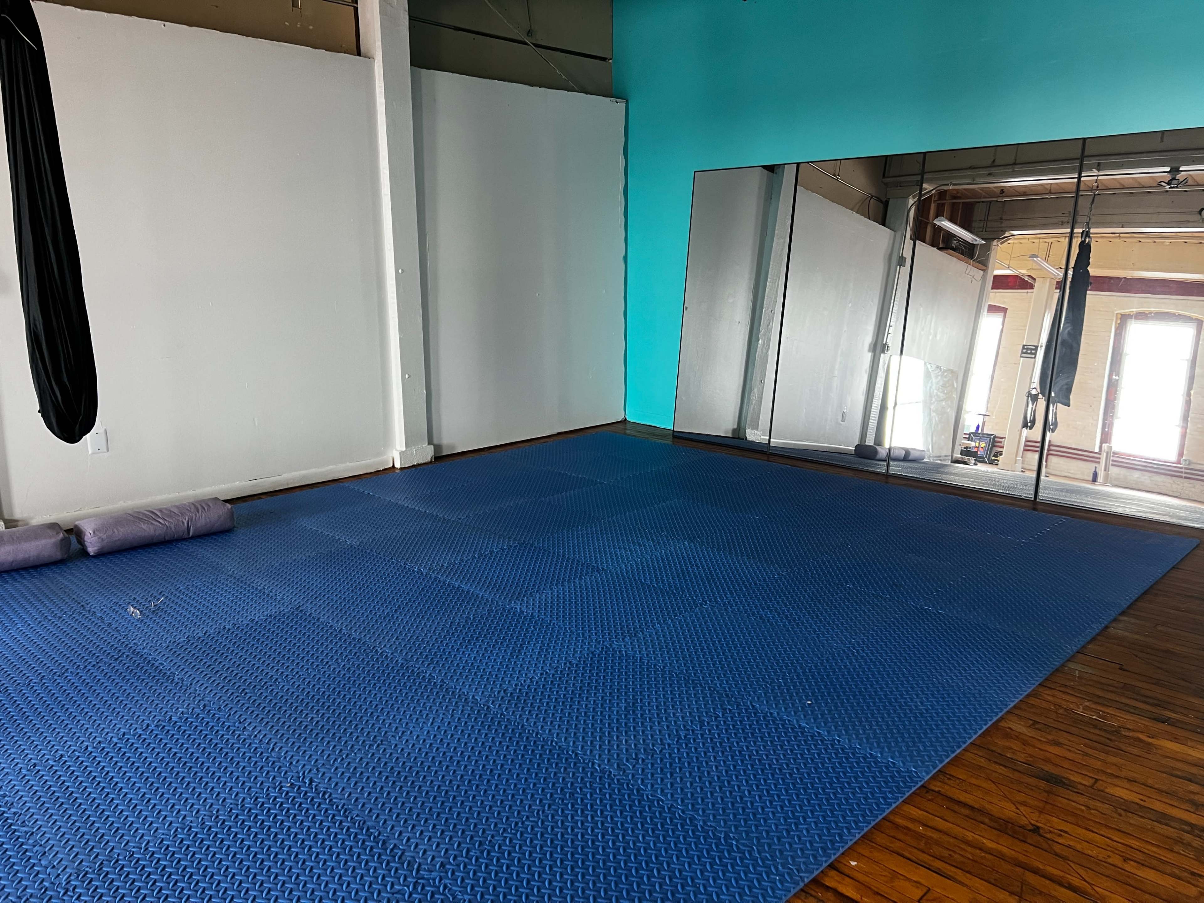 The image shows a spacious, empty room with a blue floor mat and a large mirror along one wall.