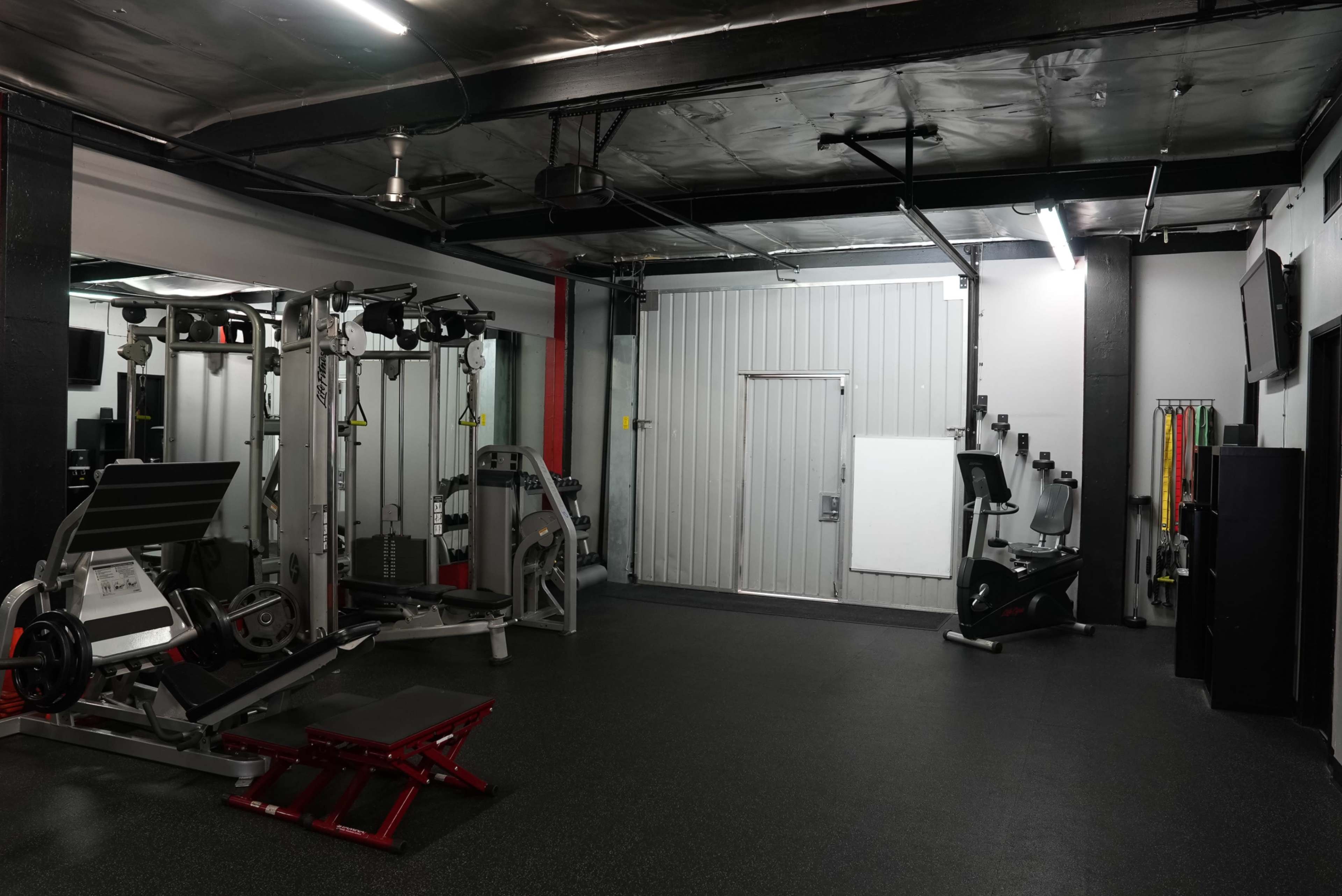 A well-equipped gym space containing weight machines, a stationary bike, and exercise bands along the wall.