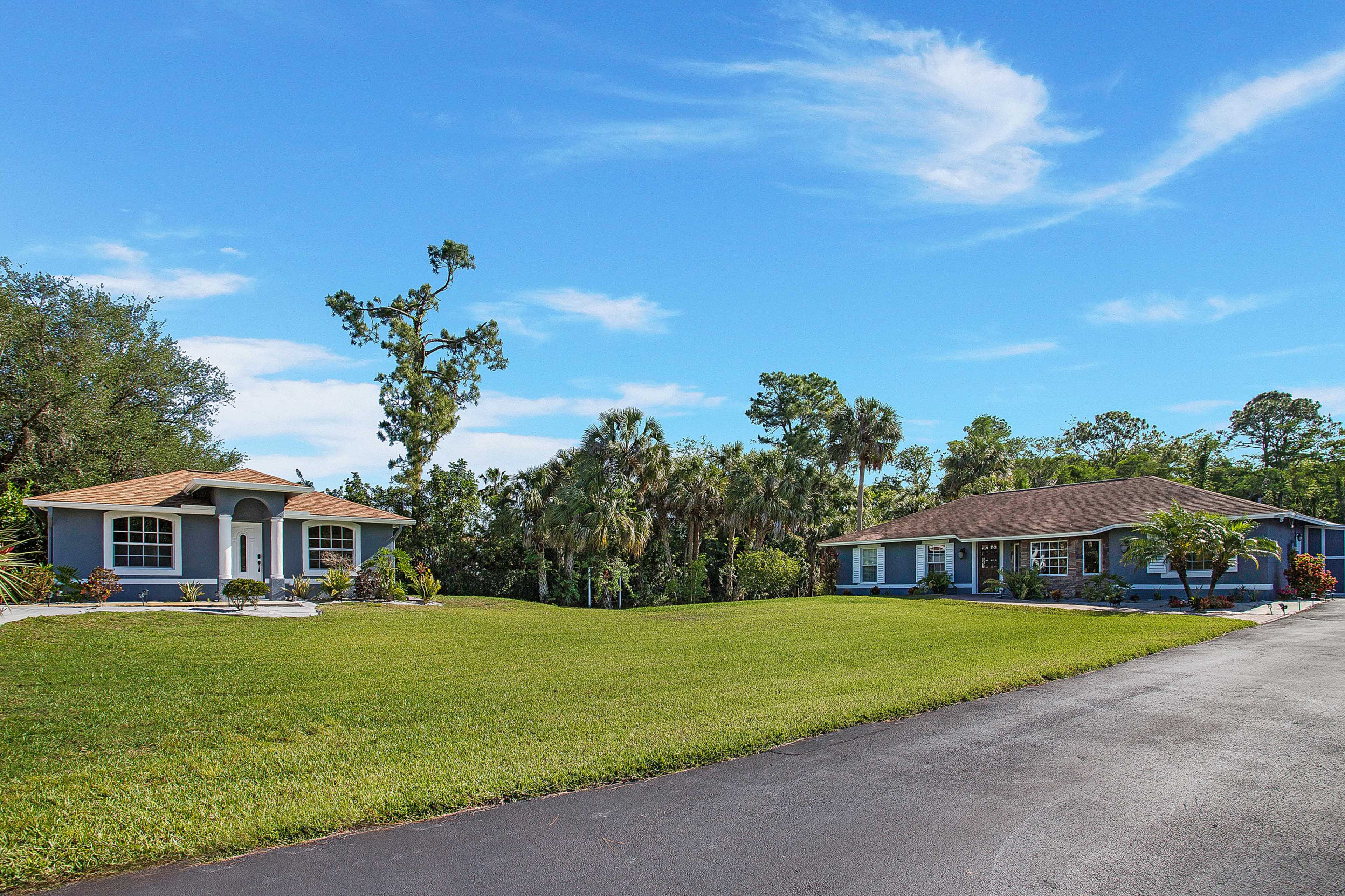 Two residential houses set on a grassy area with trees and palm plants in the background.