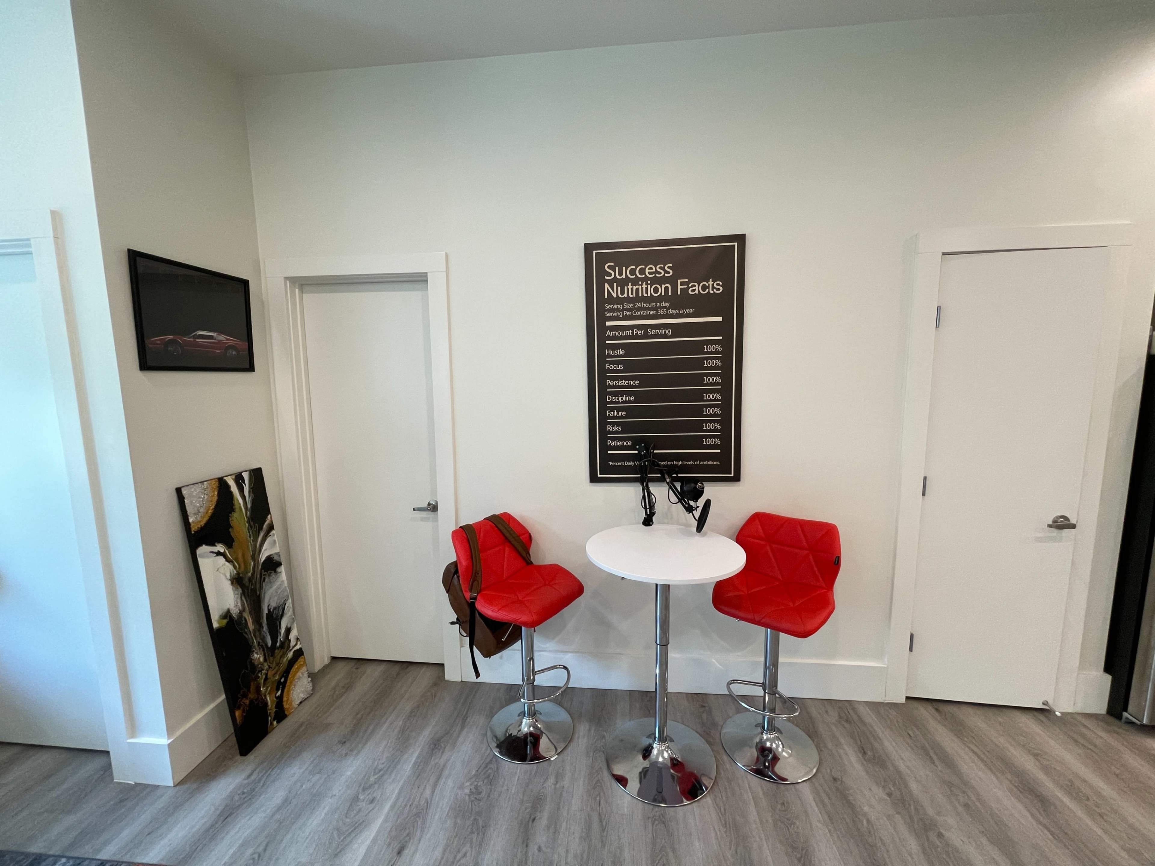 A small interior space with two red bar stools and a round table, featuring a wall-mounted chart labeled "Success Nutrition Facts" and two doors.