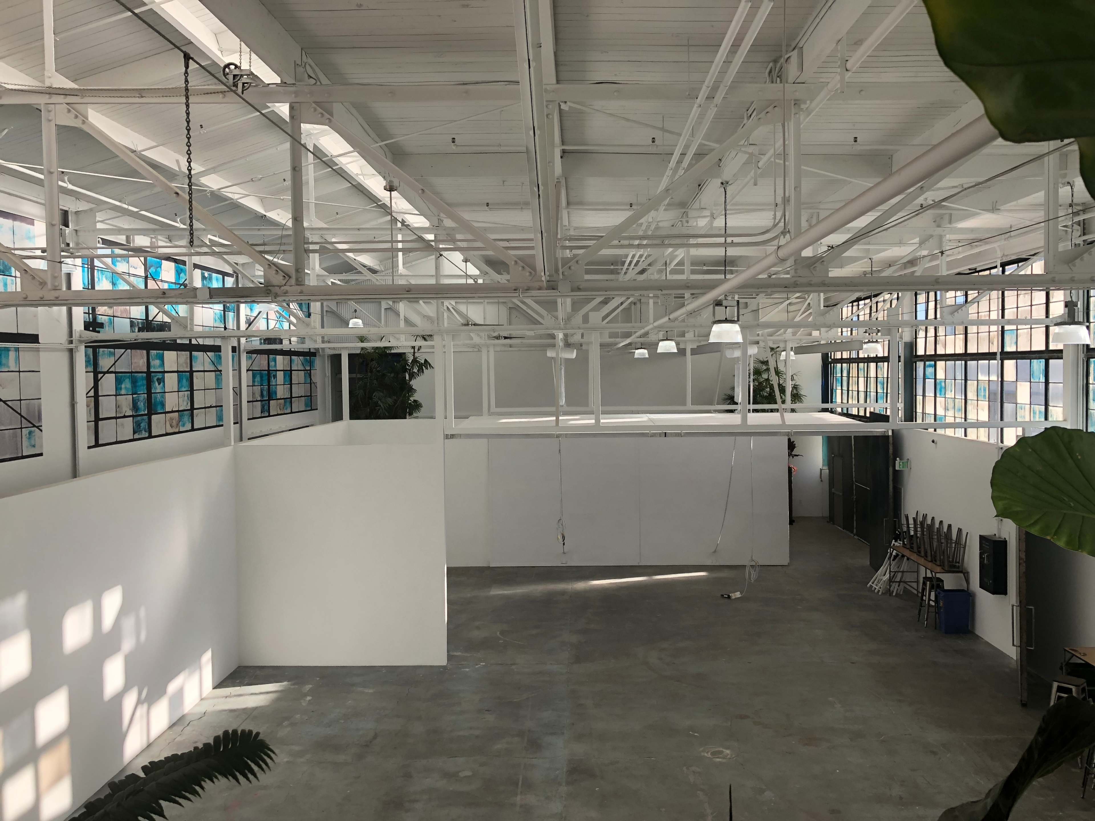 An empty industrial-style space with high ceilings, large windows, and white walls.