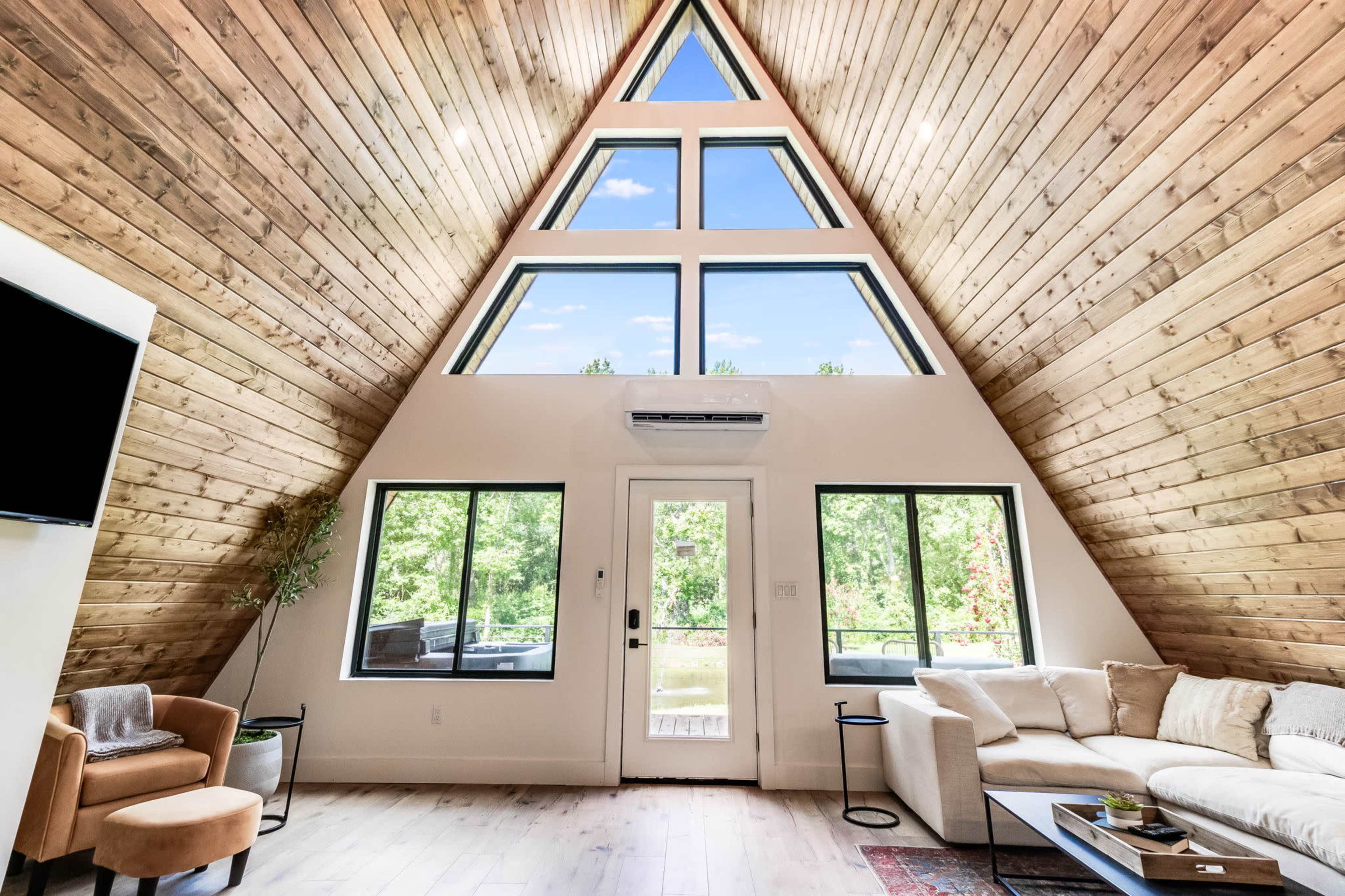 The interior of a modern A-frame cabin features large triangular windows, wooden walls, and a cozy seating area.