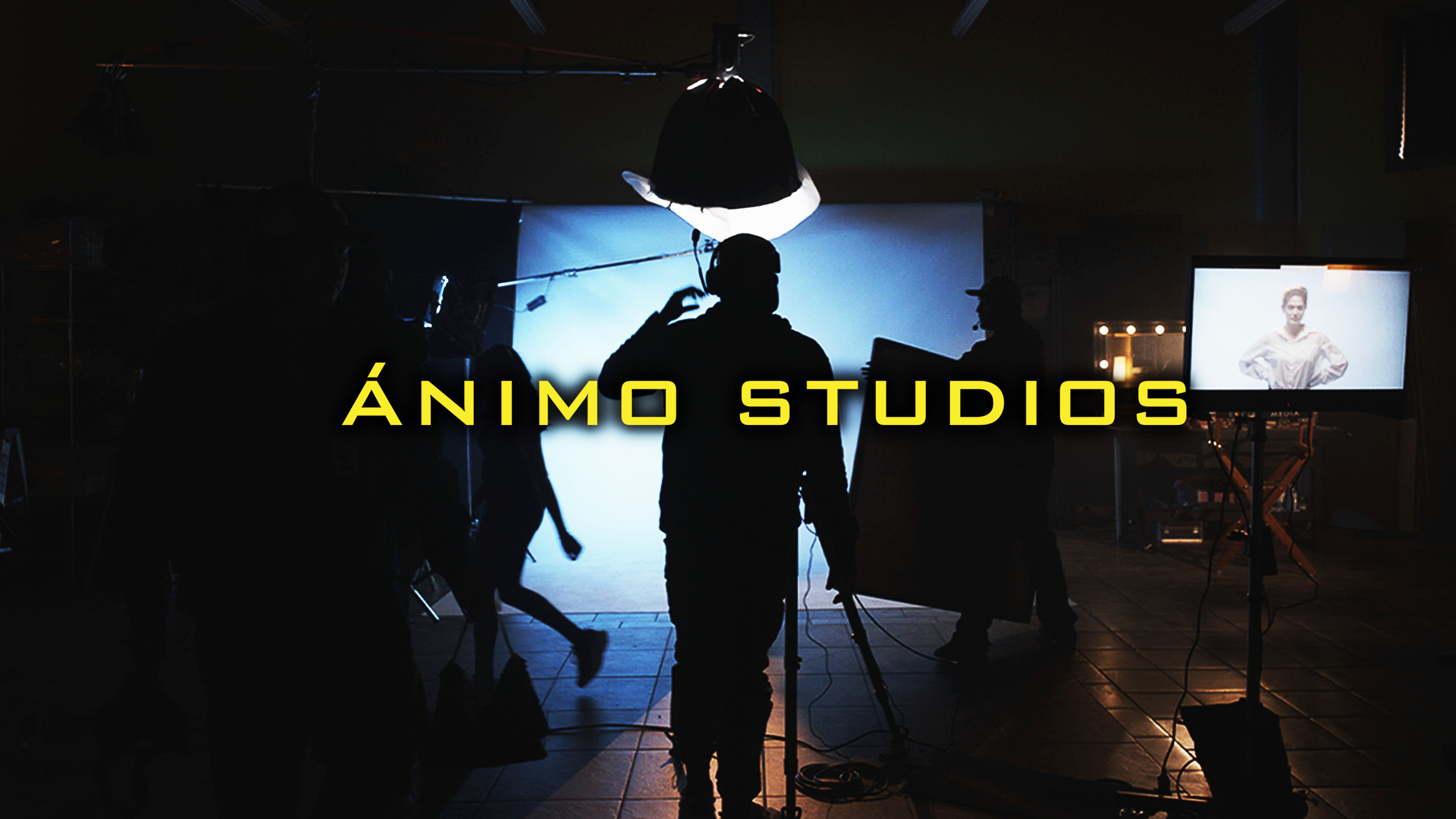 A film studio scene shows silhouetted figures preparing for a shoot, with a spotlight illuminating the set and a monitor displaying a model's image.