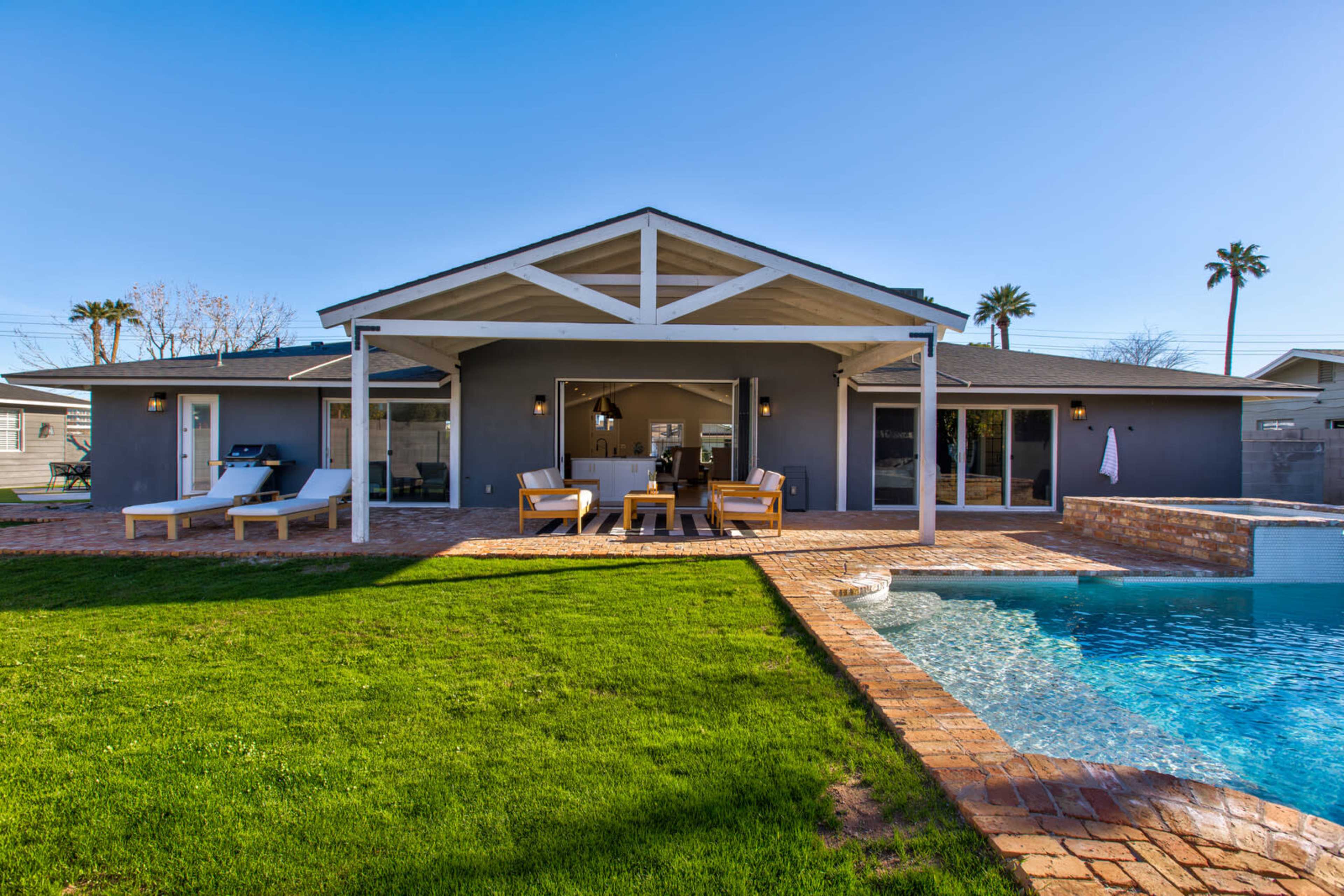 A modern house with a patio and swimming pool is surrounded by a green lawn and palm trees.