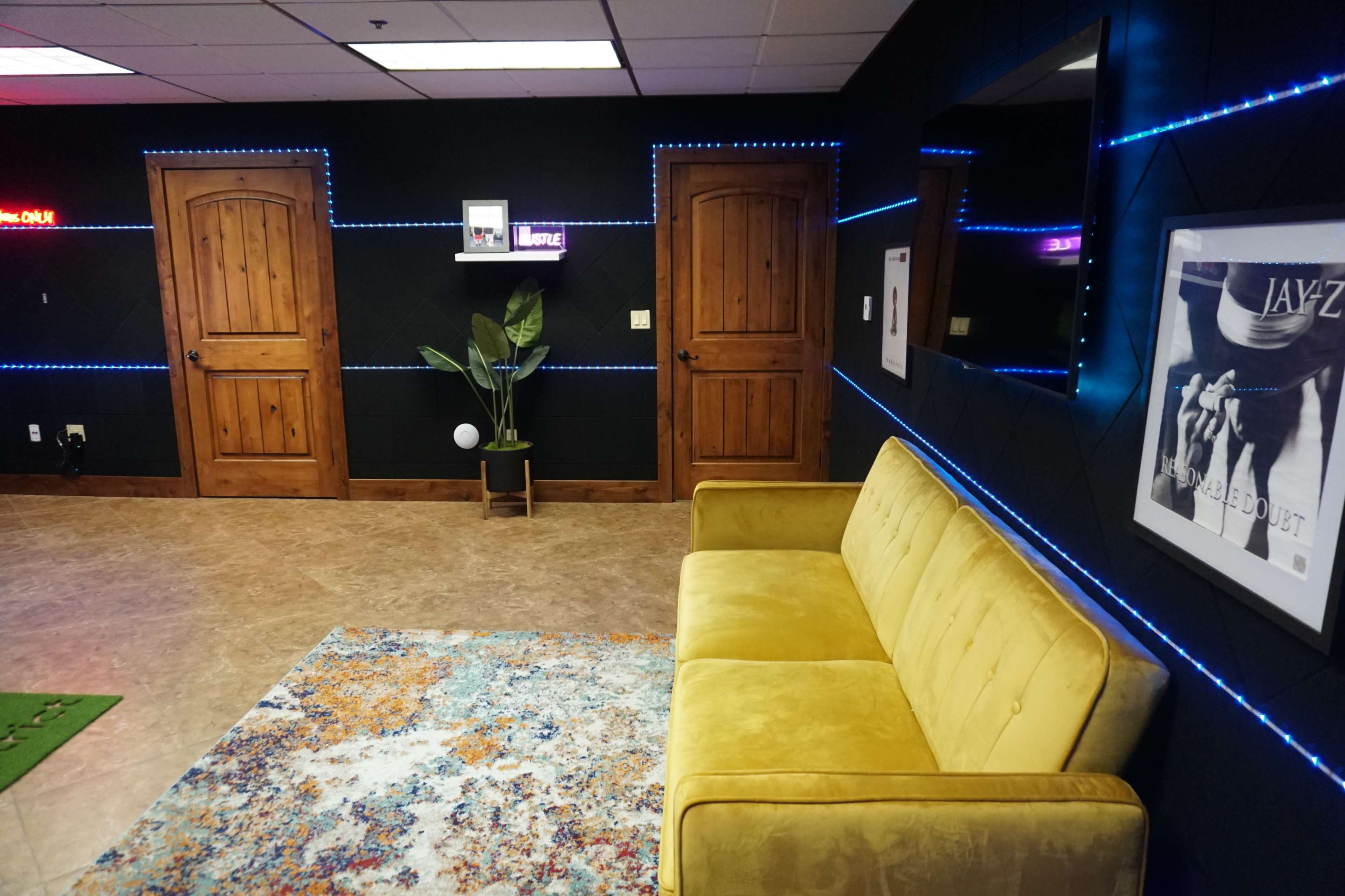 A modern room with a yellow sofa, a colorful area rug, two wooden doors, and ambient blue lighting along the walls.