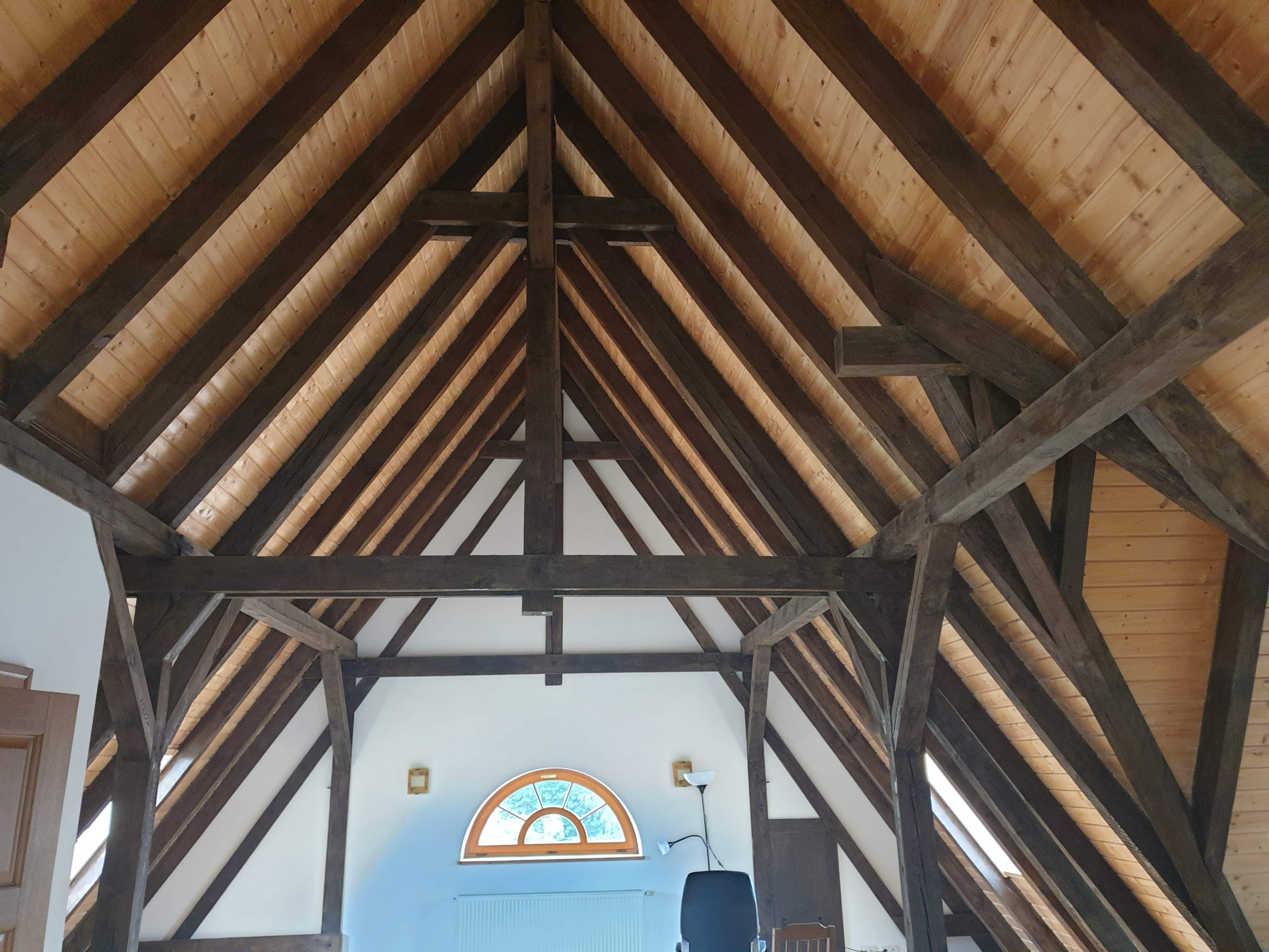 A spacious room with a high wooden beam ceiling and a large arched window.