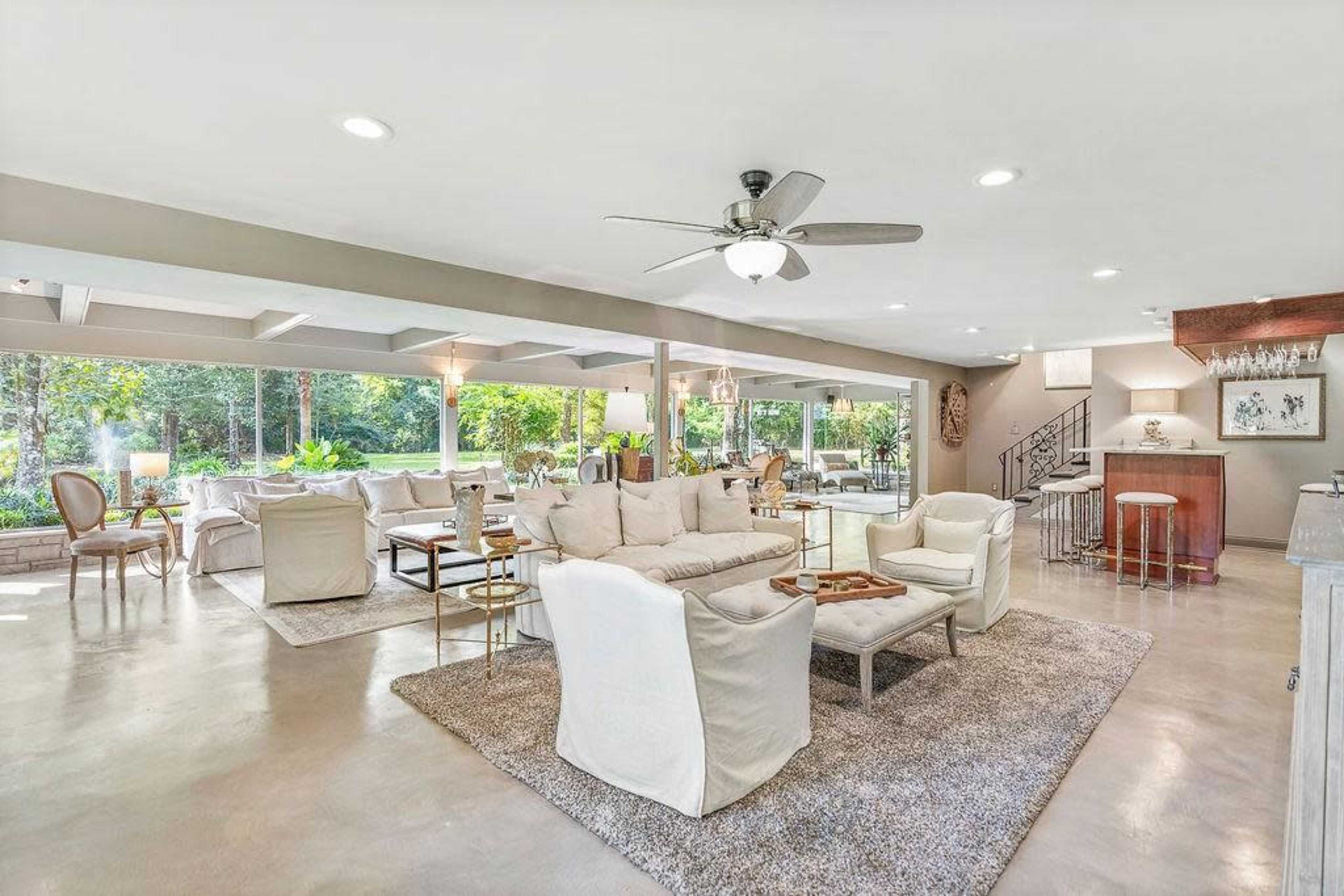 The open living area features a combination of white furniture, large glass windows, and a polished concrete floor, creating a bright and spacious environment.