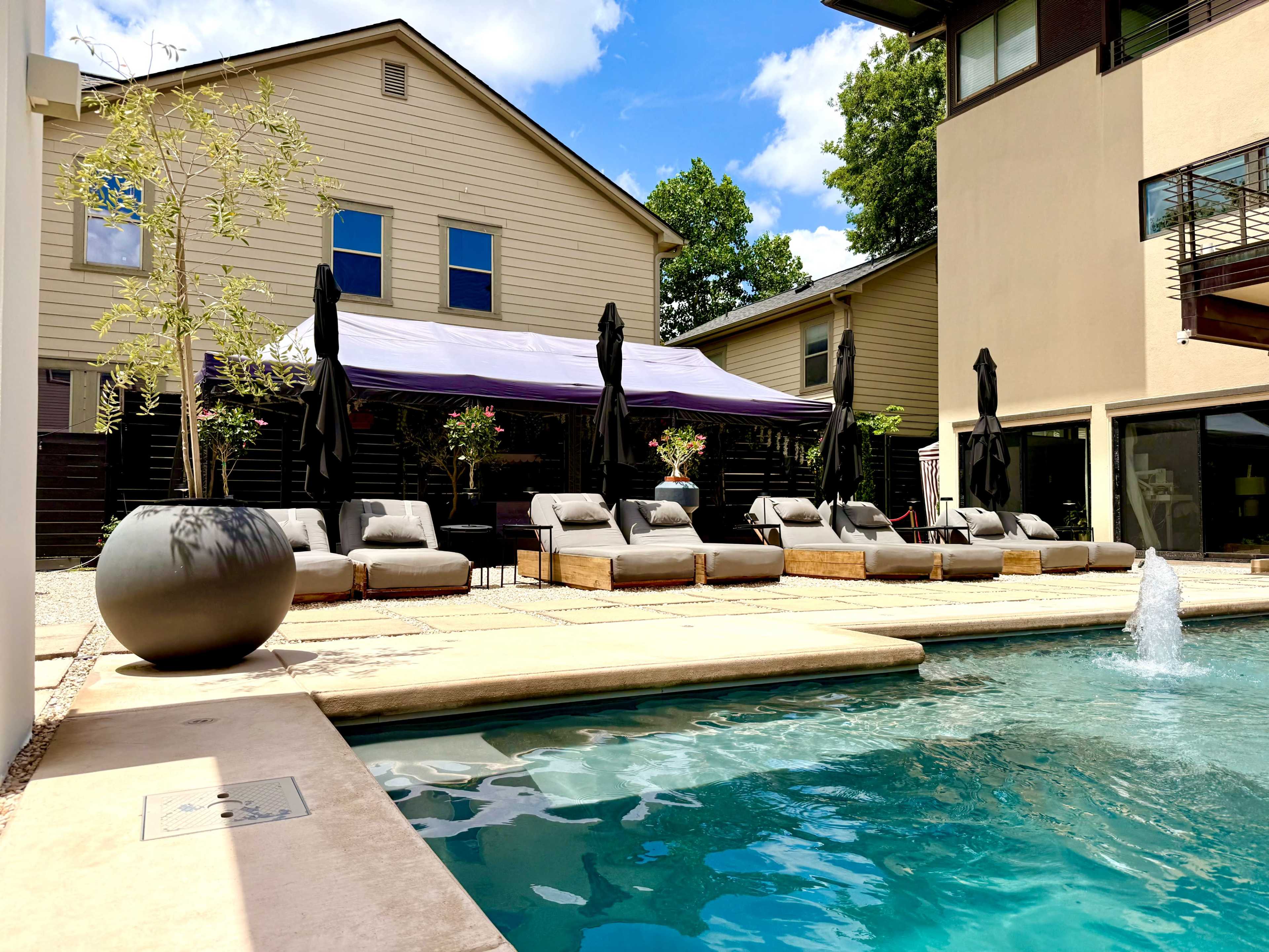 The image shows a swimming pool area with several lounge chairs and umbrellas next to a building.