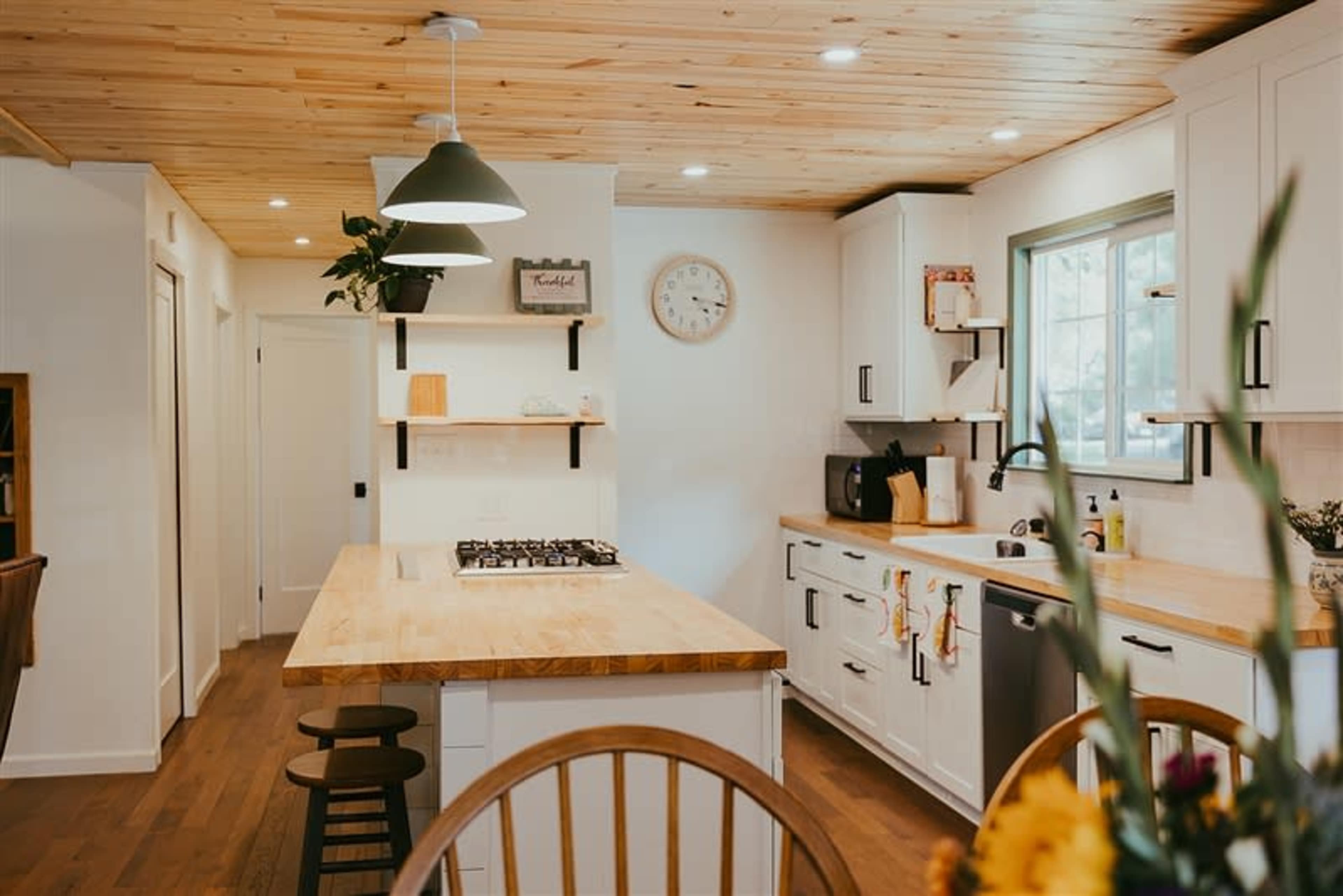 The image shows a modern kitchen with a wooden island, white cabinetry, and a window above the sink.