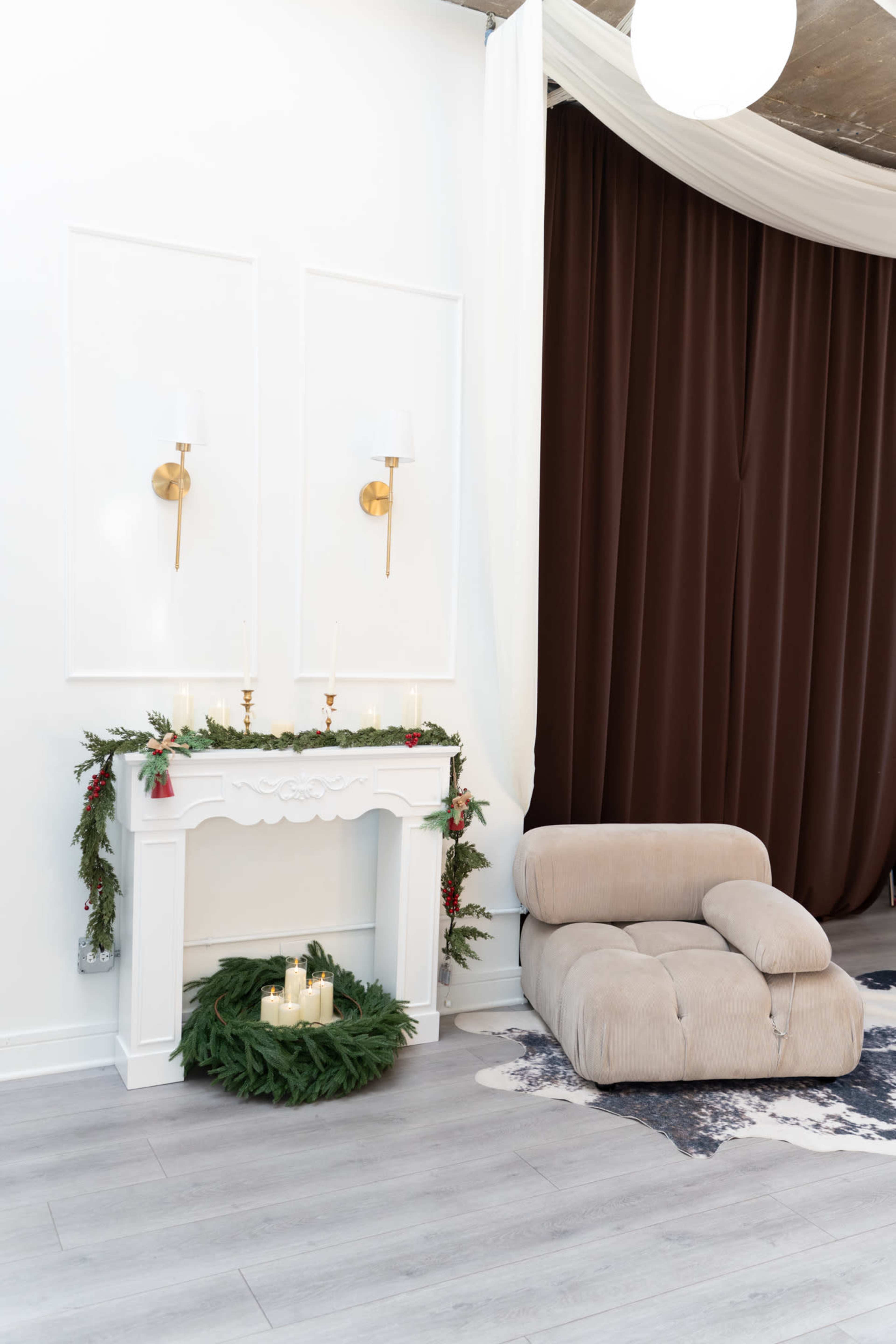The image features a modern living space with a white decorative mantel adorned with greenery, two wall sconces, and a beige armchair beside a dark curtain.