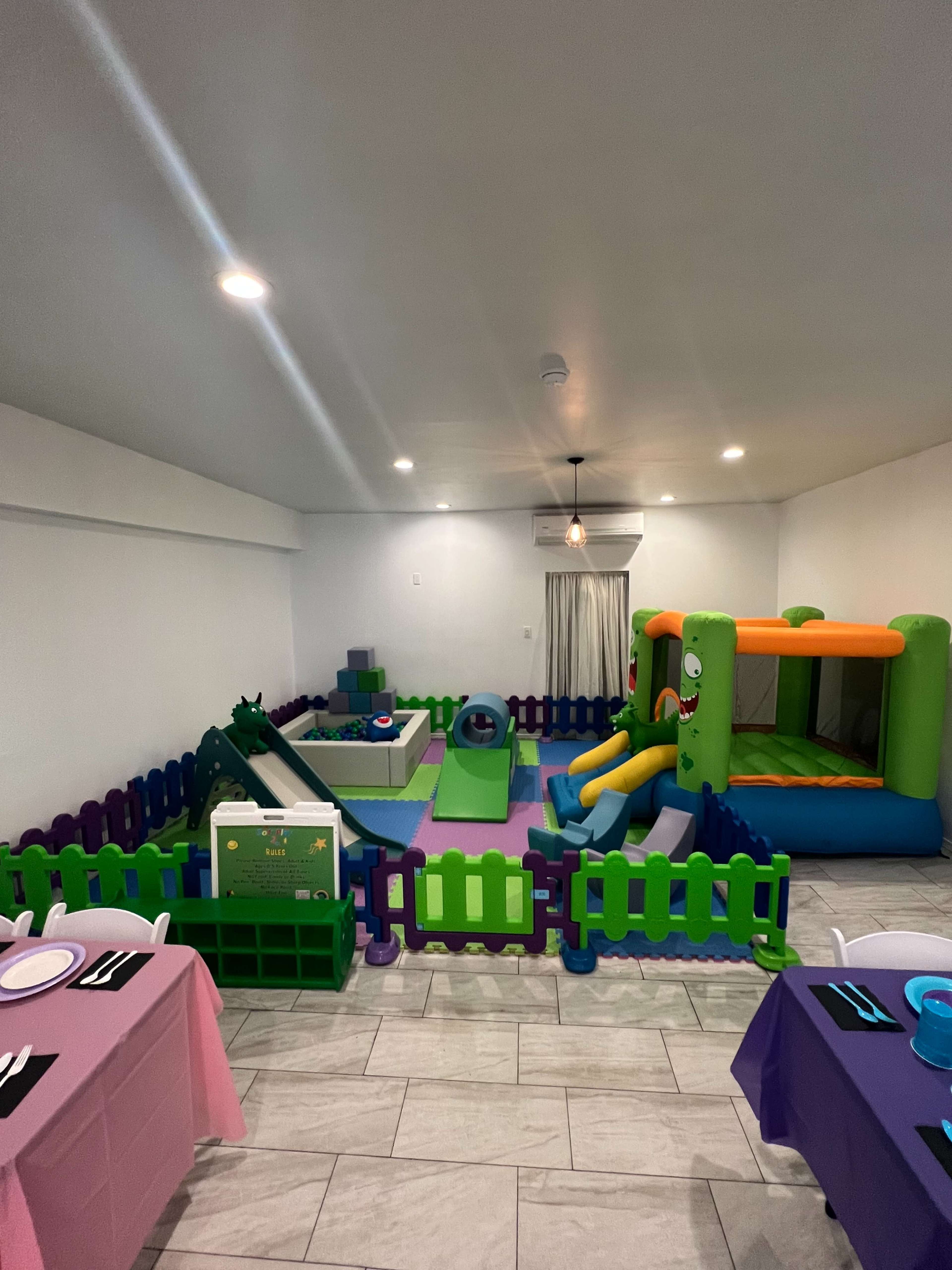 An indoor play area equipped with colorful inflatable toys, a bouncing castle, and various play structures surrounded by plastic fencing.