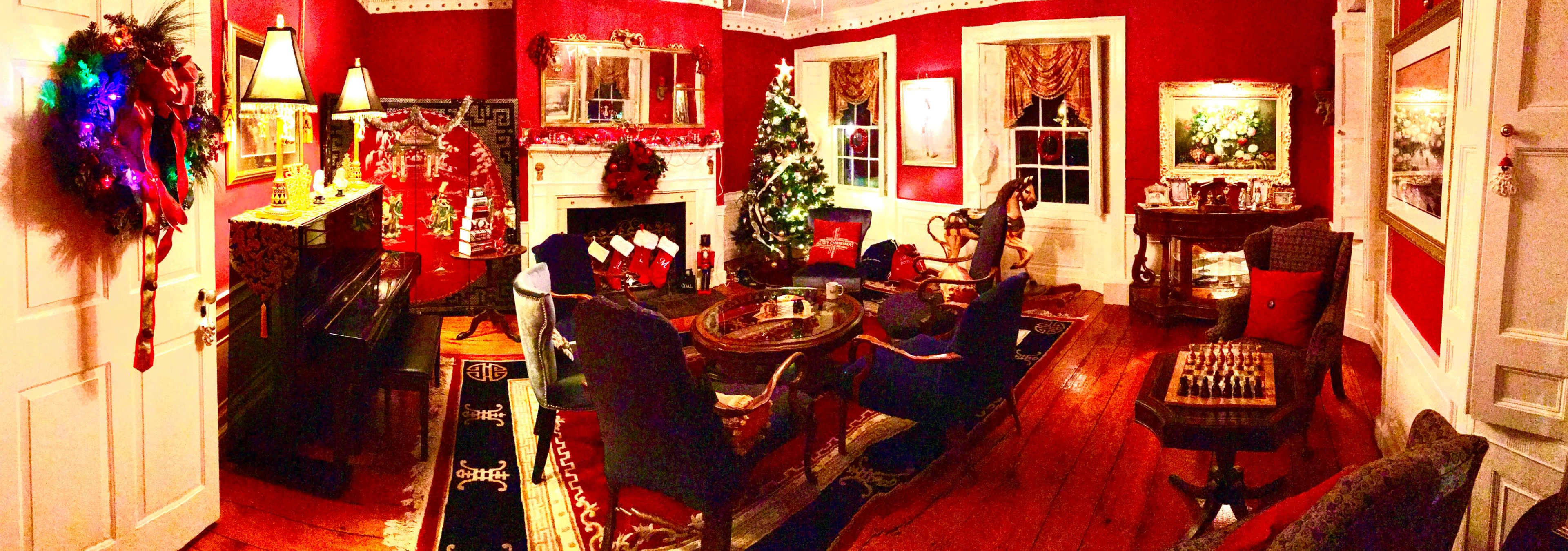 A festive living room decorated in red, featuring a Christmas tree, a fireplace, a piano, and various holiday decorations.
