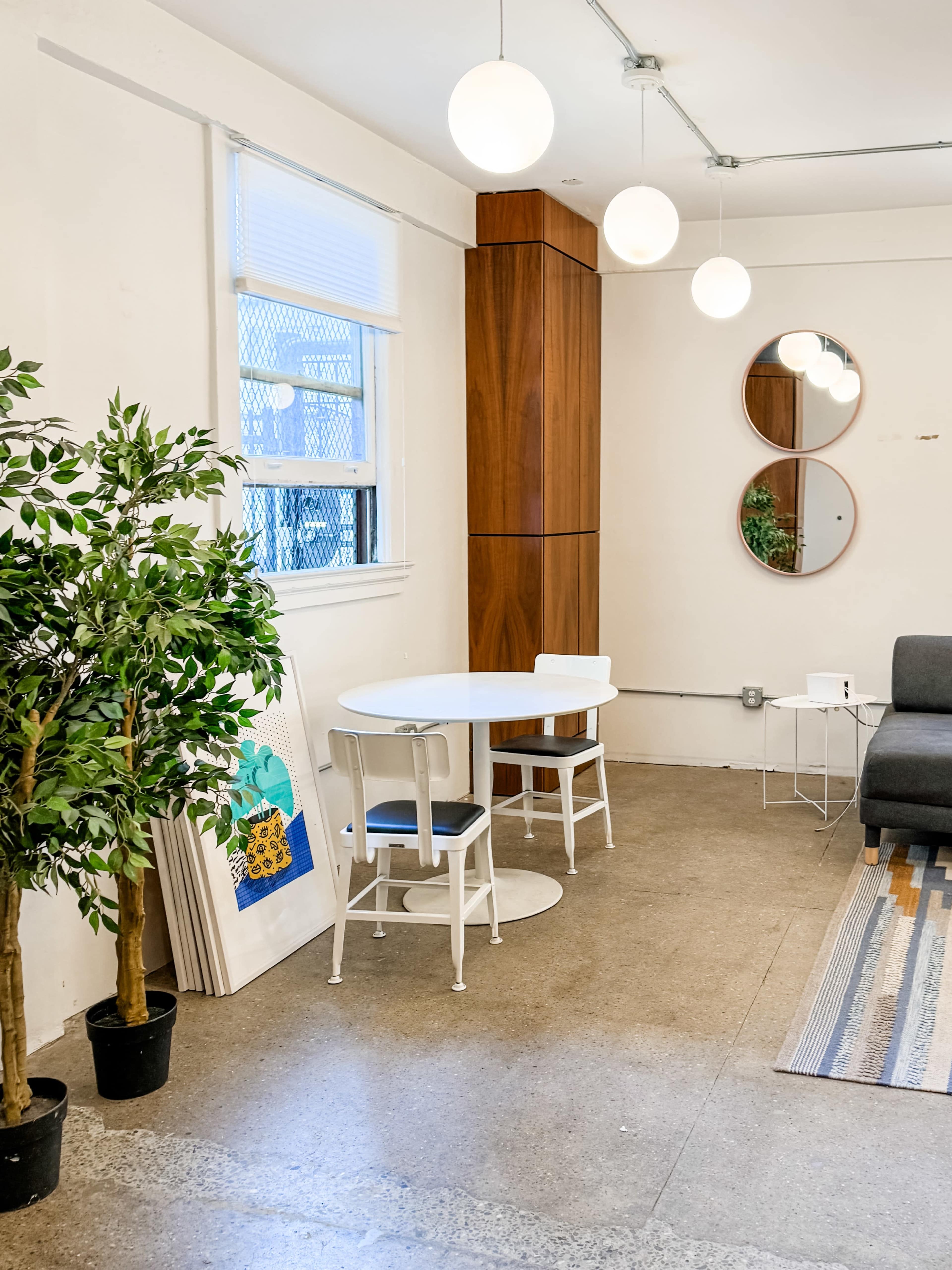 A small, modern room features a round white table with chairs, two circular mirrors, and plants beside a gray sofa.