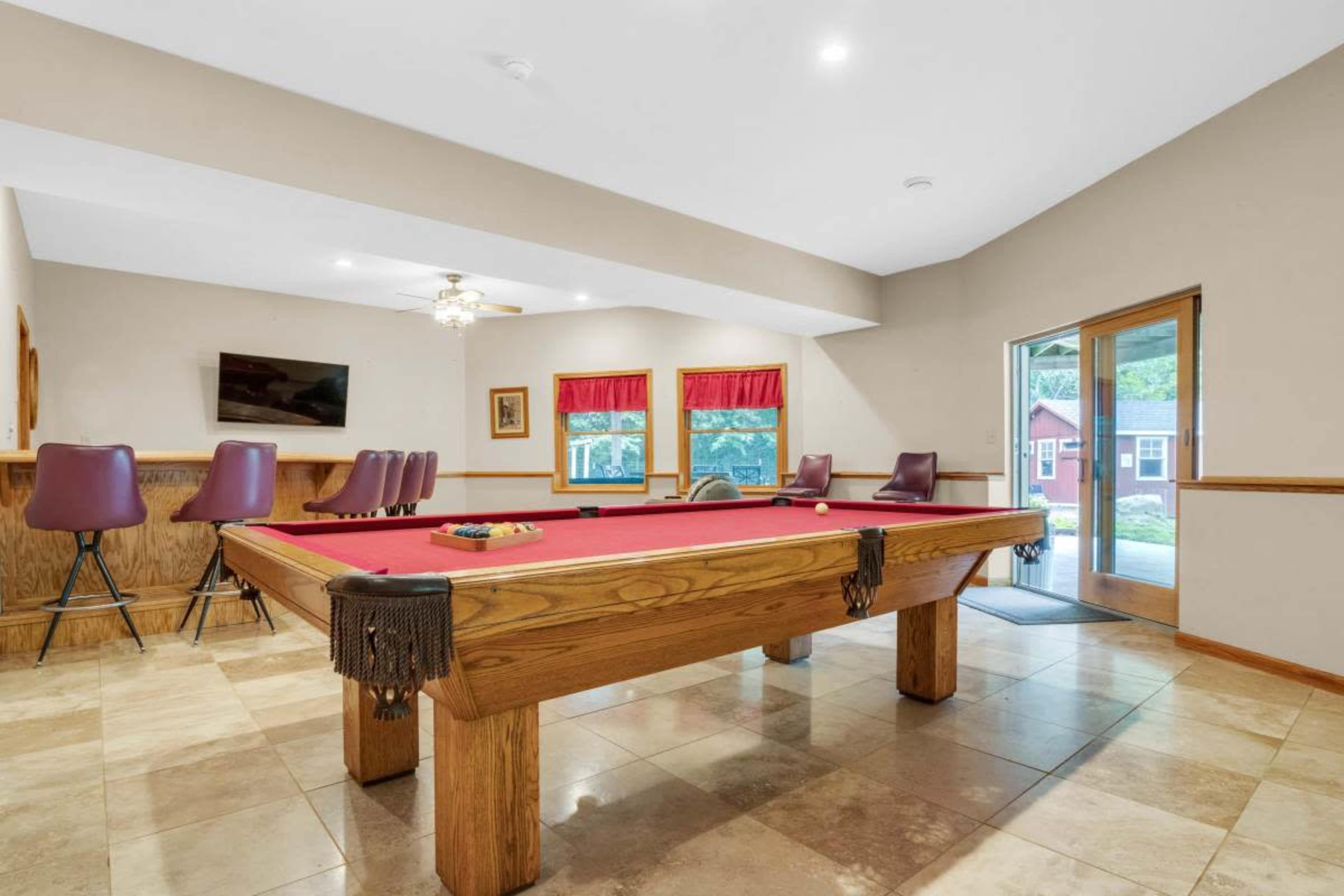 The room features a pool table surrounded by bar stools, with a sliding door that leads outside.