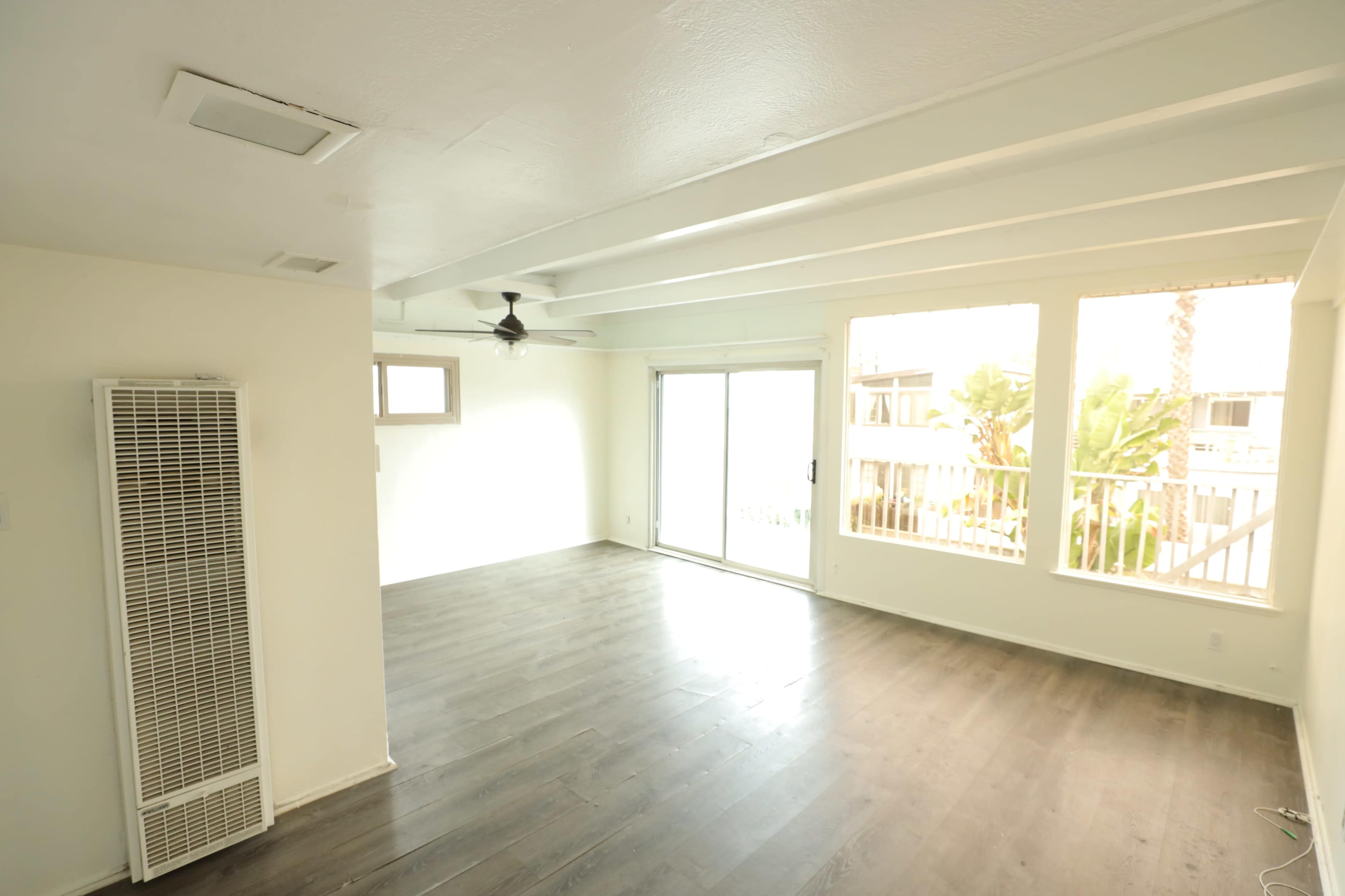 The image shows a bright living room with a ceiling fan, large windows, and light-colored walls.
