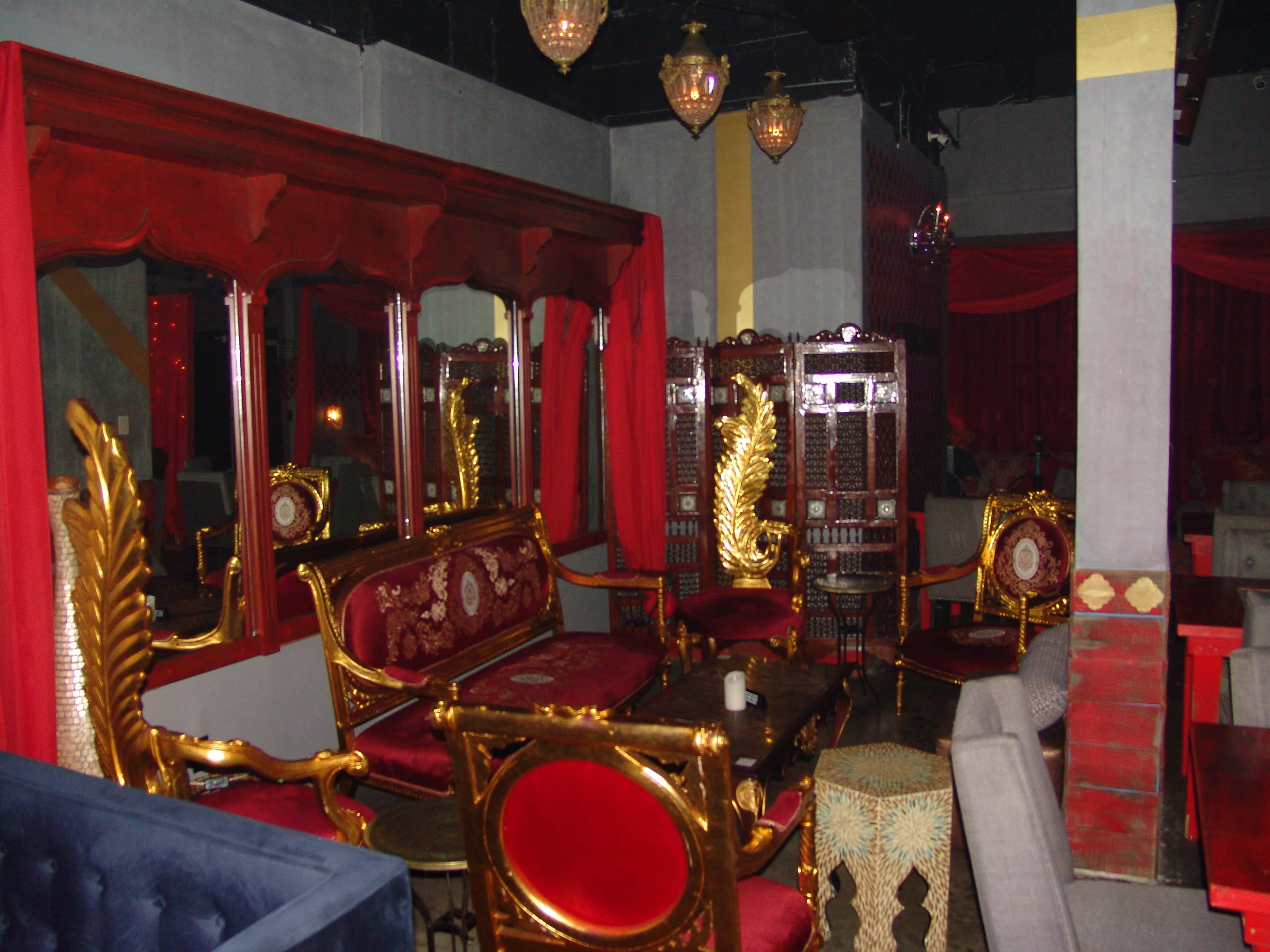 The image shows a dimly lit lounge with ornate gold-accented seating, red curtains, and decorative screens.
