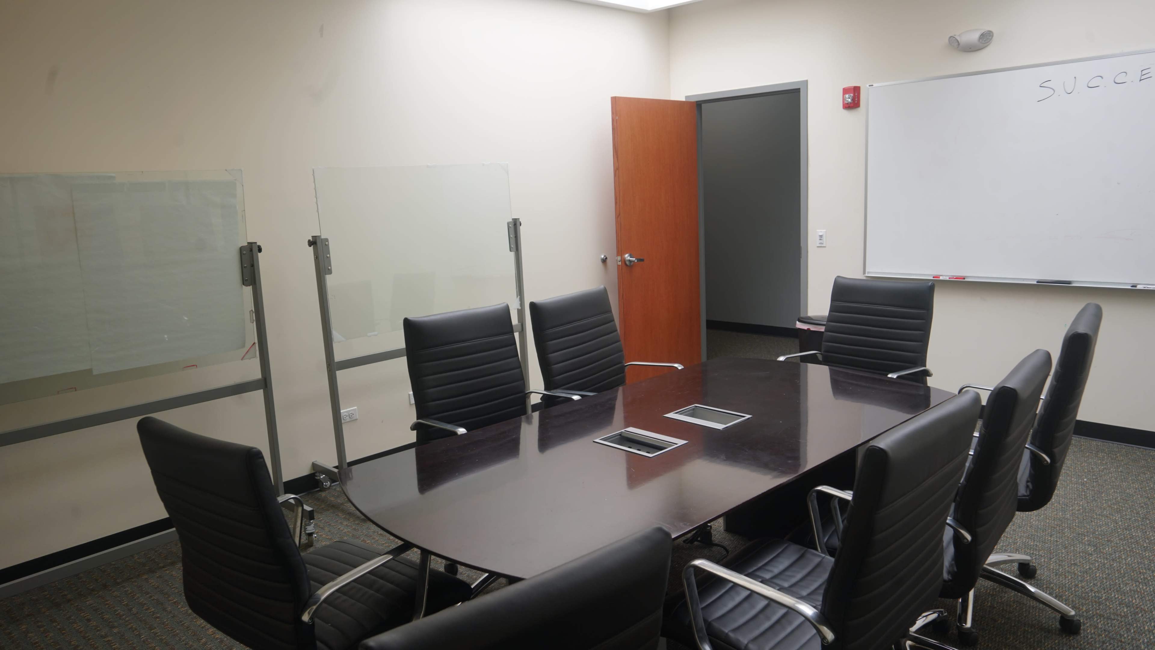 A conference room with a large oval table surrounded by black leather chairs and a whiteboard on the wall.