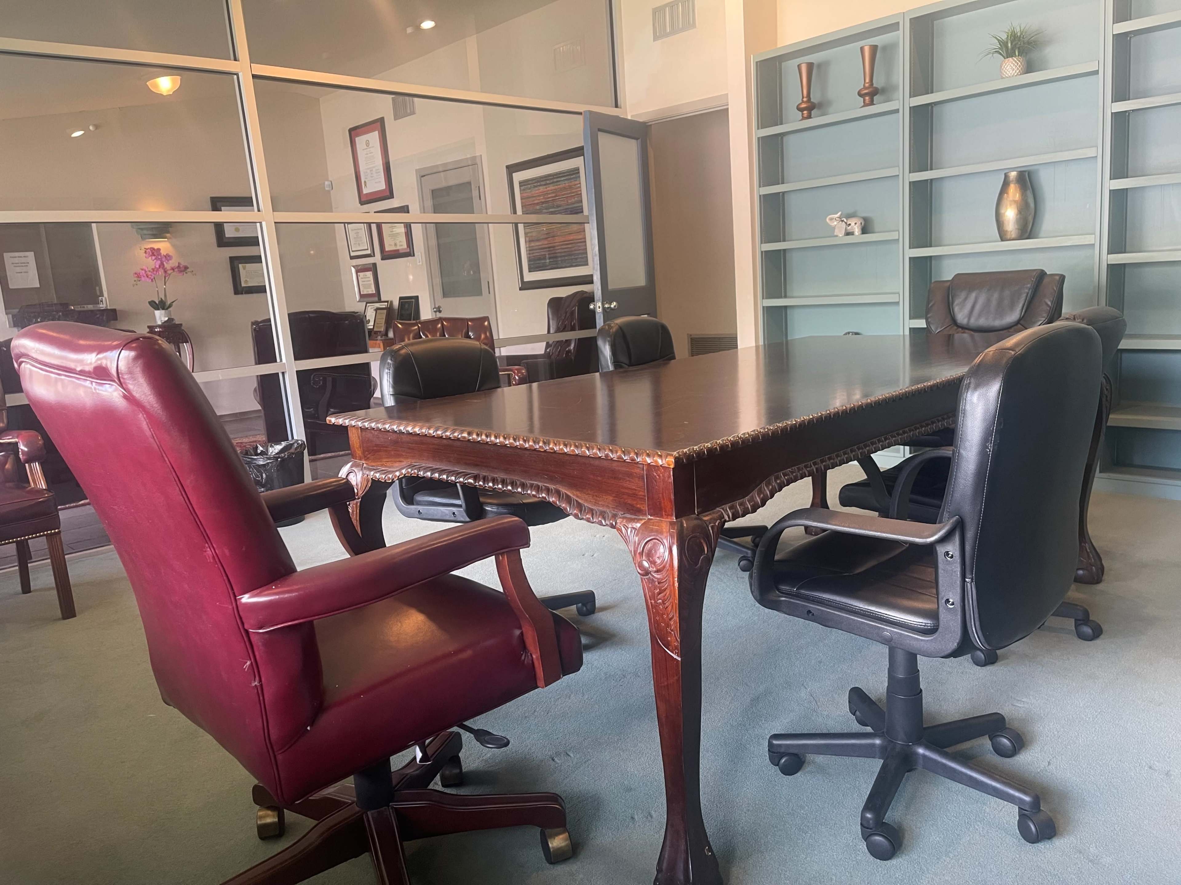 A conference table with ornate detailing is surrounded by five office chairs in a modern meeting room.
