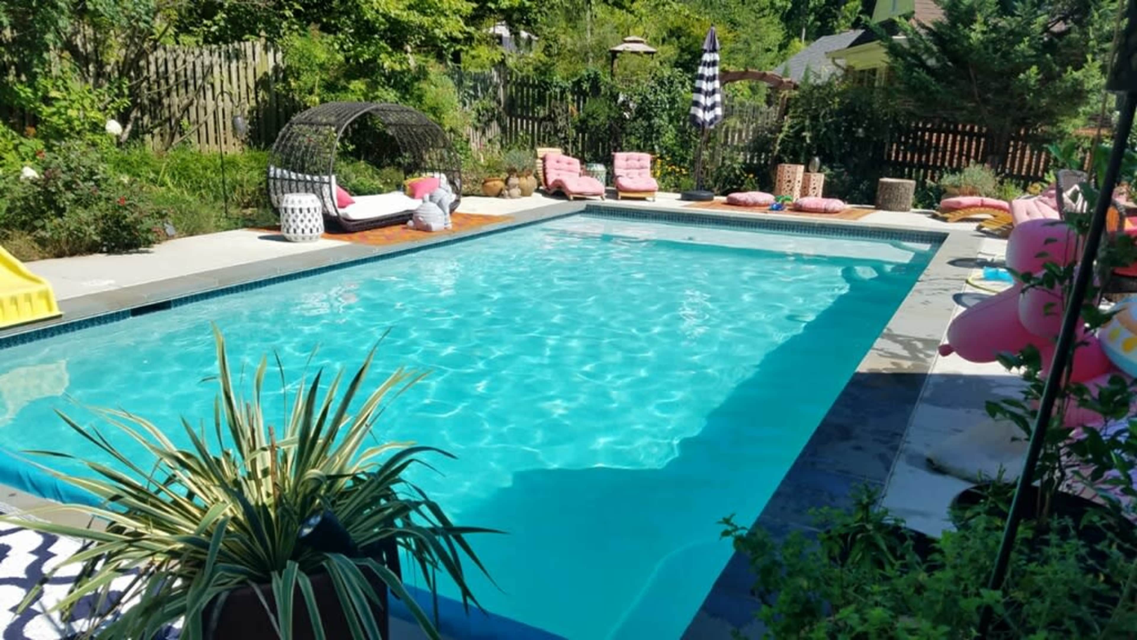 A clear swimming pool surrounded by lounge chairs, poolside decorations, and lush greenery.