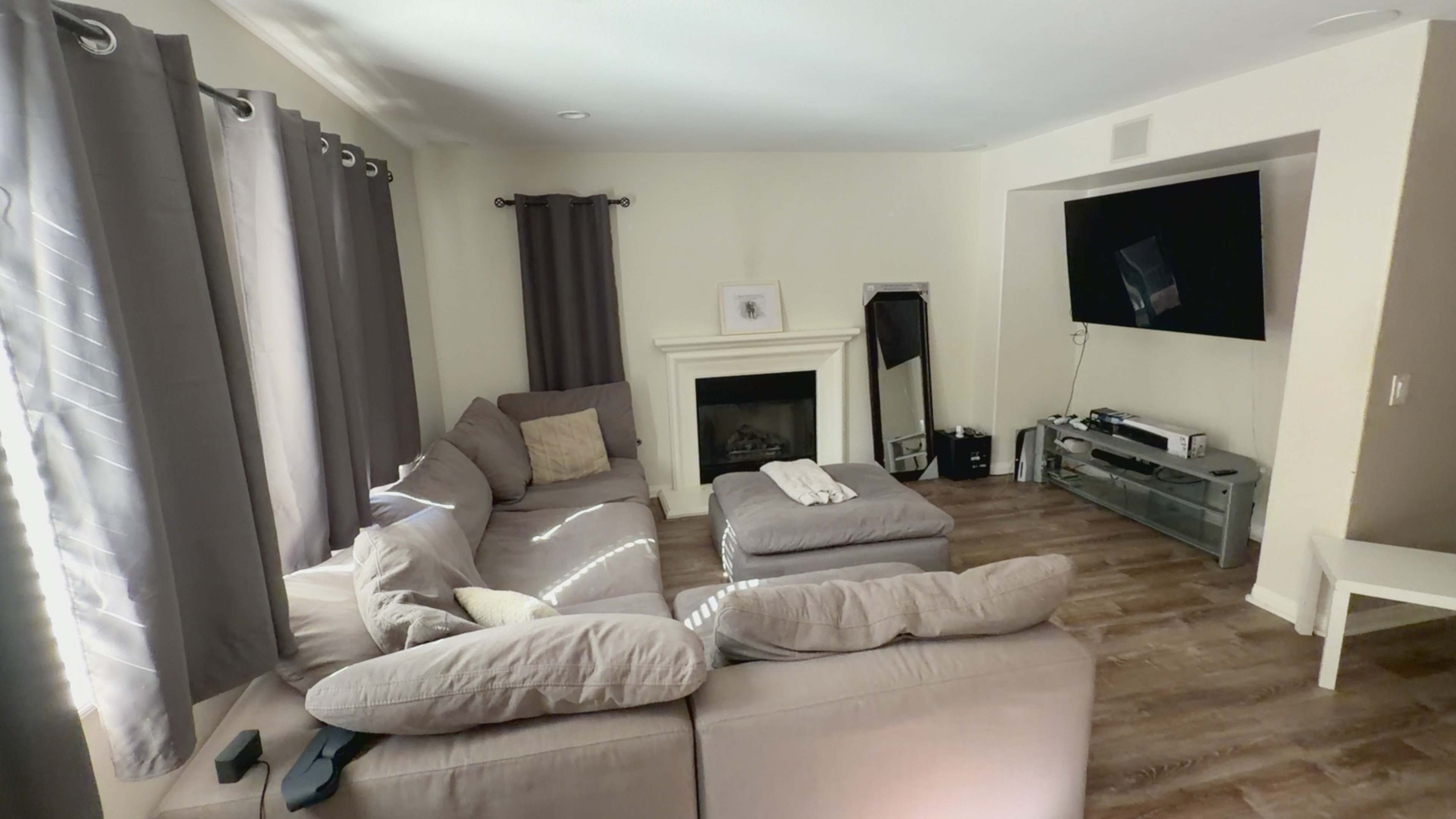 The living room features a sectional sofa, a fireplace, and a television mounted on the wall with a wooden floor.