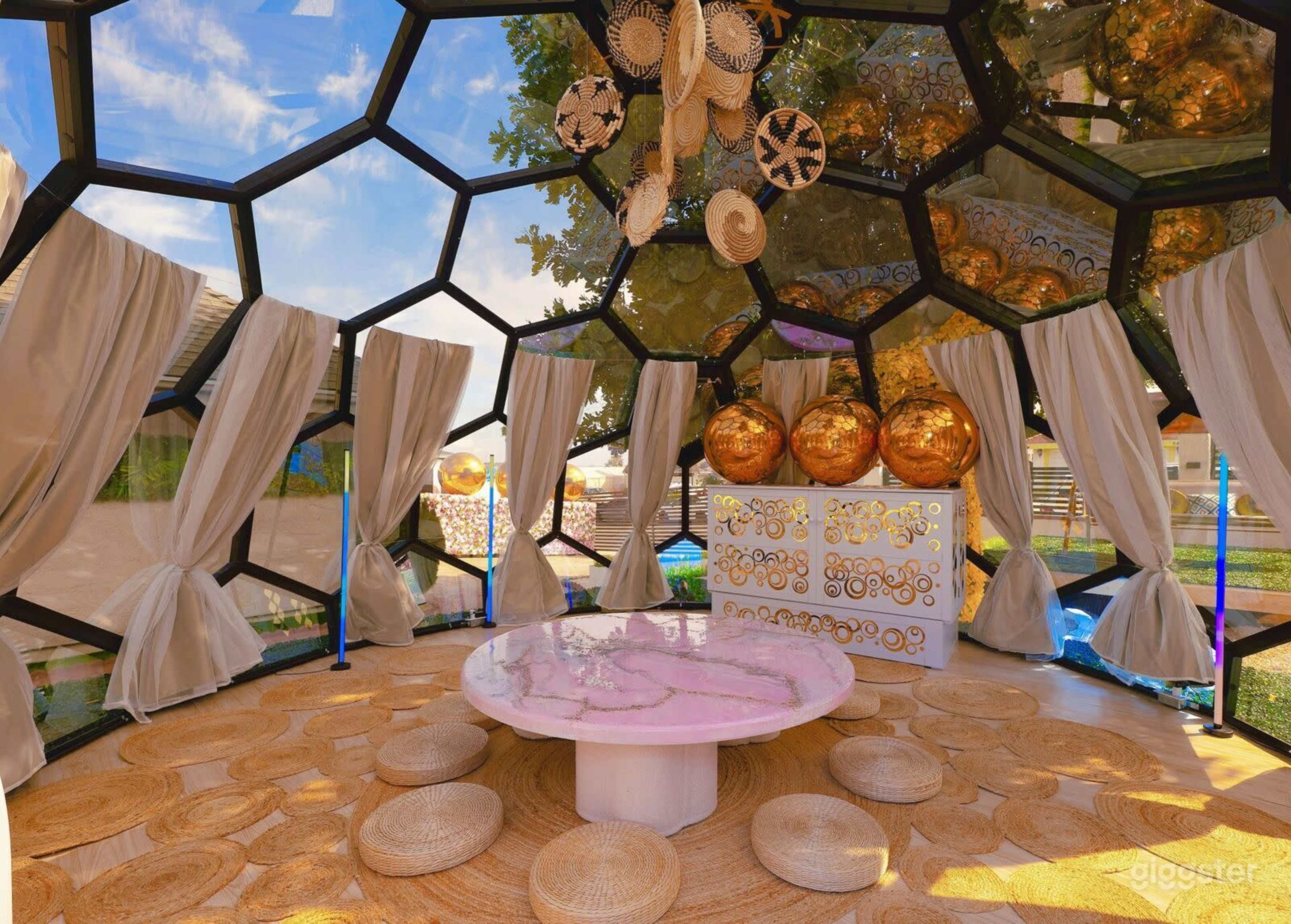 The image shows a geodesic dome interior featuring a round table, circular seating, and decorative hanging elements, with large windows allowing natural light to fill the space.