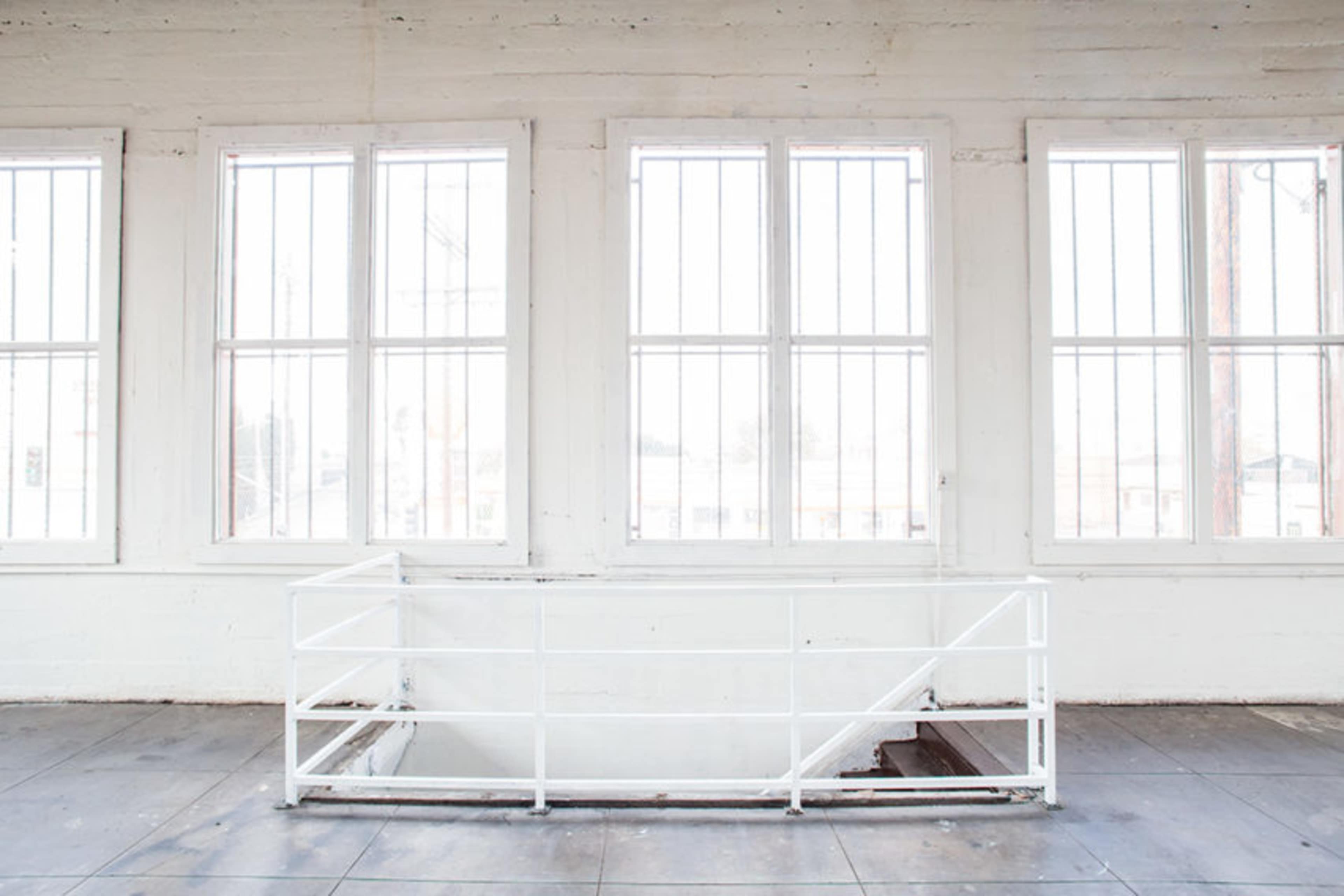 A white-railed staircase leads down into a brightly lit, empty room with large windows.