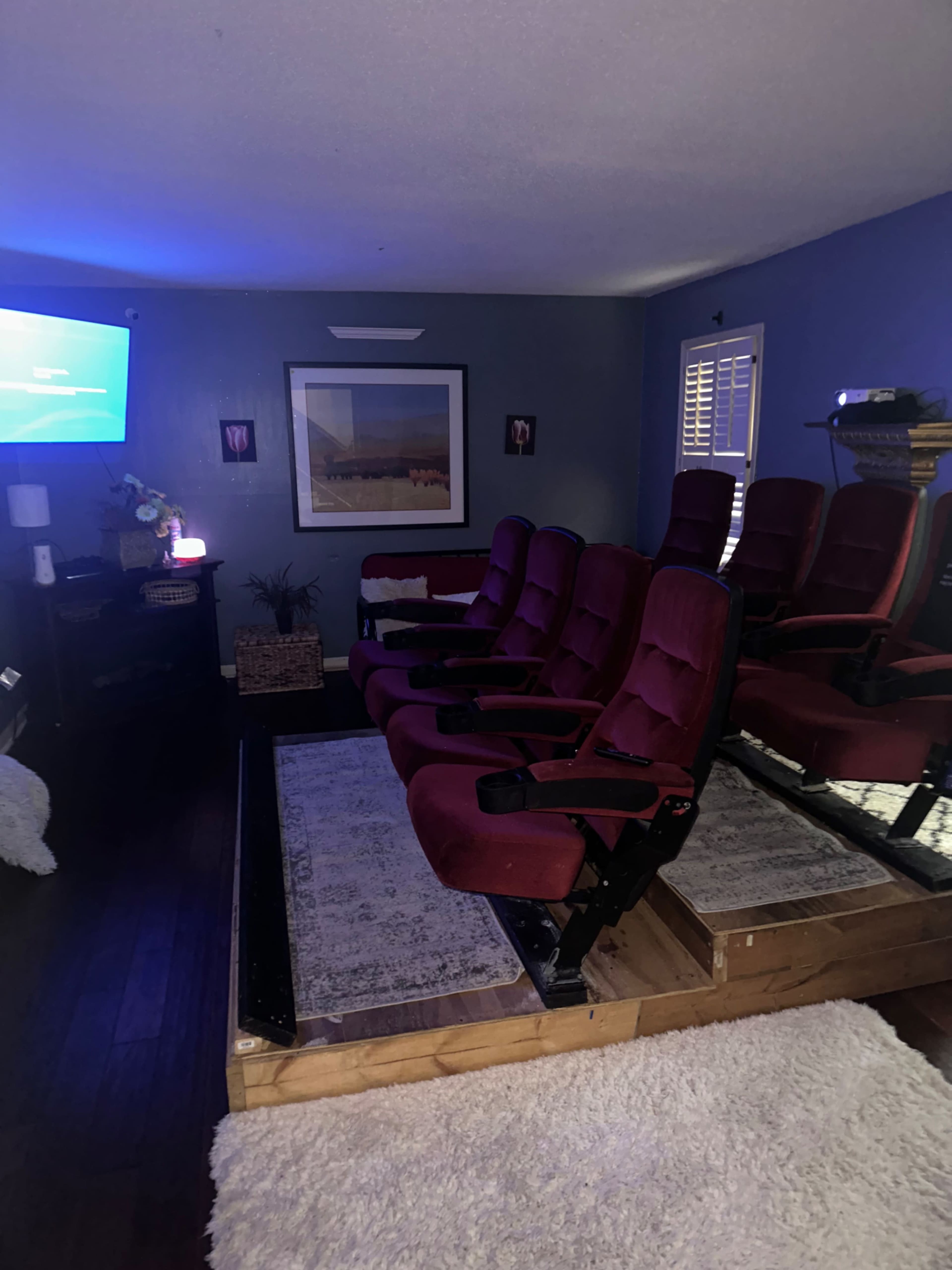 A home theater setup with red reclining seats arranged on a wooden platform, facing a wall-mounted television.