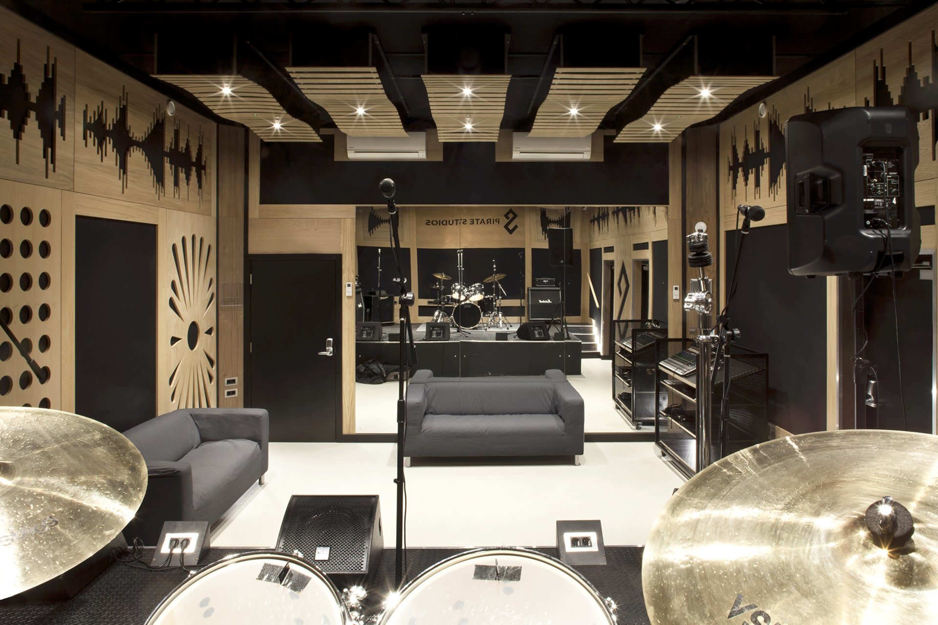 A modern recording studio featuring a drum set in the foreground and soundproof walls with a mirror reflecting various musical instruments in the background.