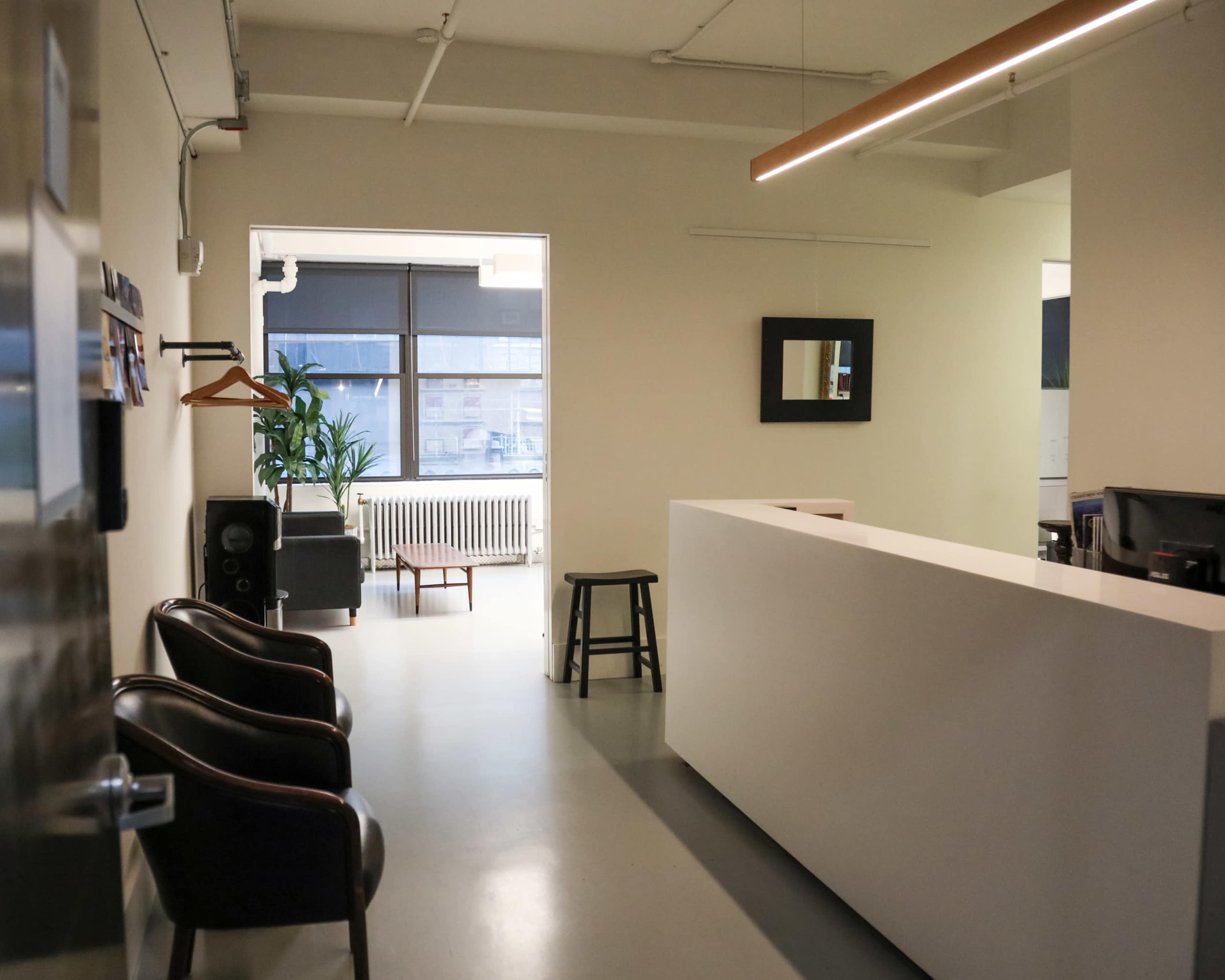 A modern, minimalistic reception area with a white desk, two dark chairs, and a large window providing natural light.