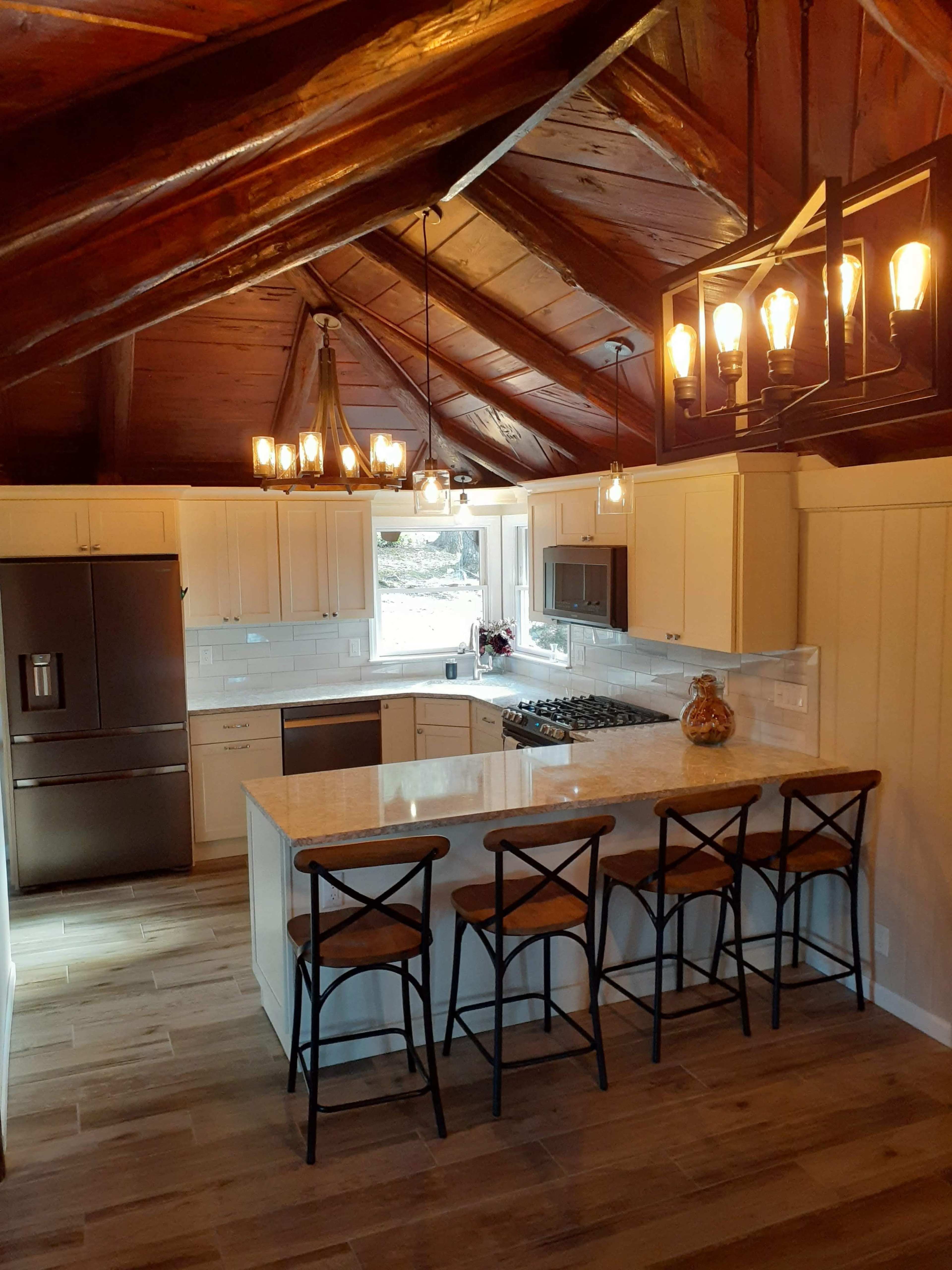 A modern kitchen features a large island with bar stools, stainless steel appliances, and wooden ceiling beams.