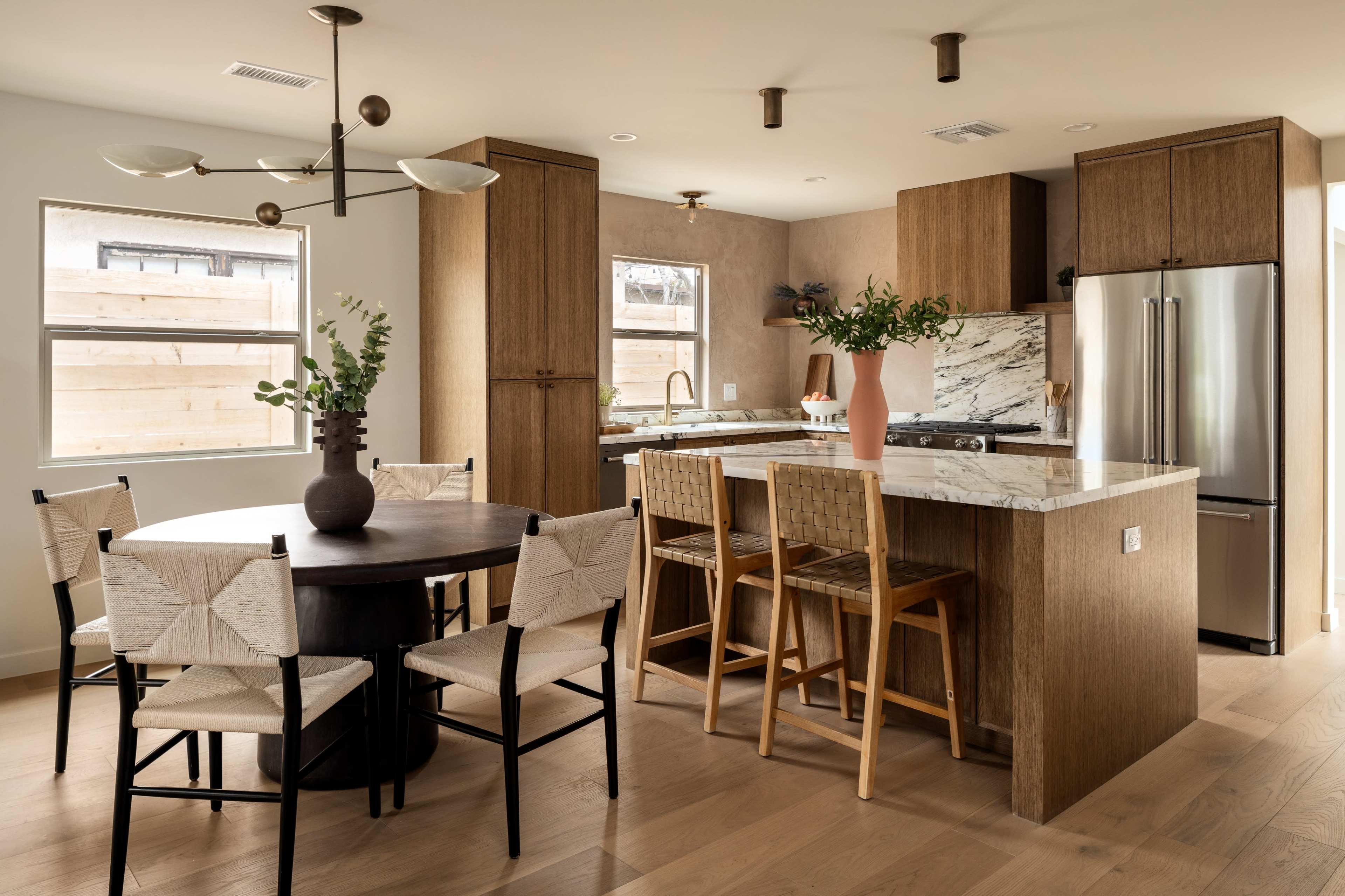 A modern kitchen and dining area featuring a round table with four chairs, a kitchen island with seating, and cabinetry in warm wood tones.