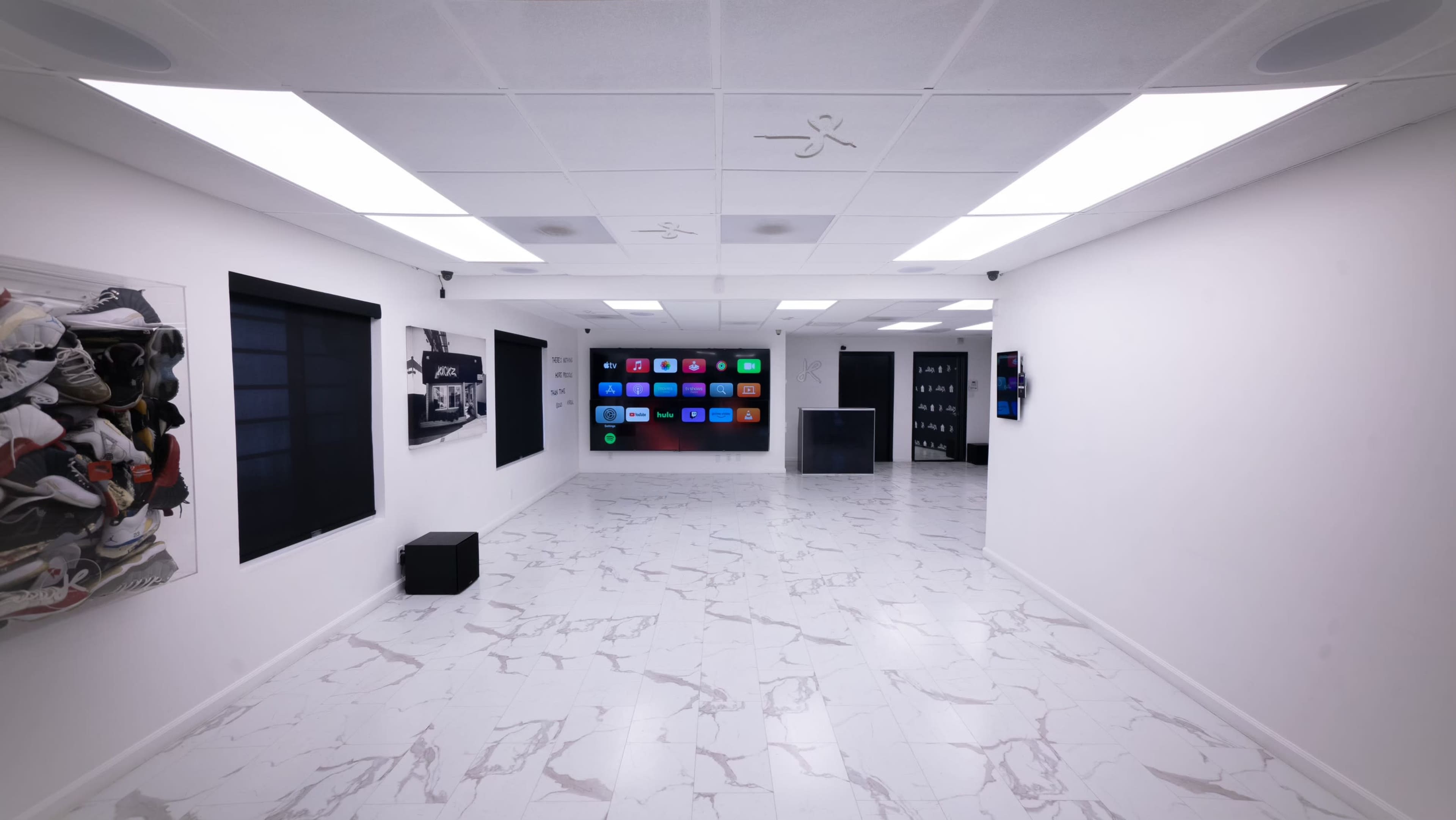 The image shows a spacious, minimalist room with white walls, a glossy tiled floor, and a large screen displaying colorful icons on one side.