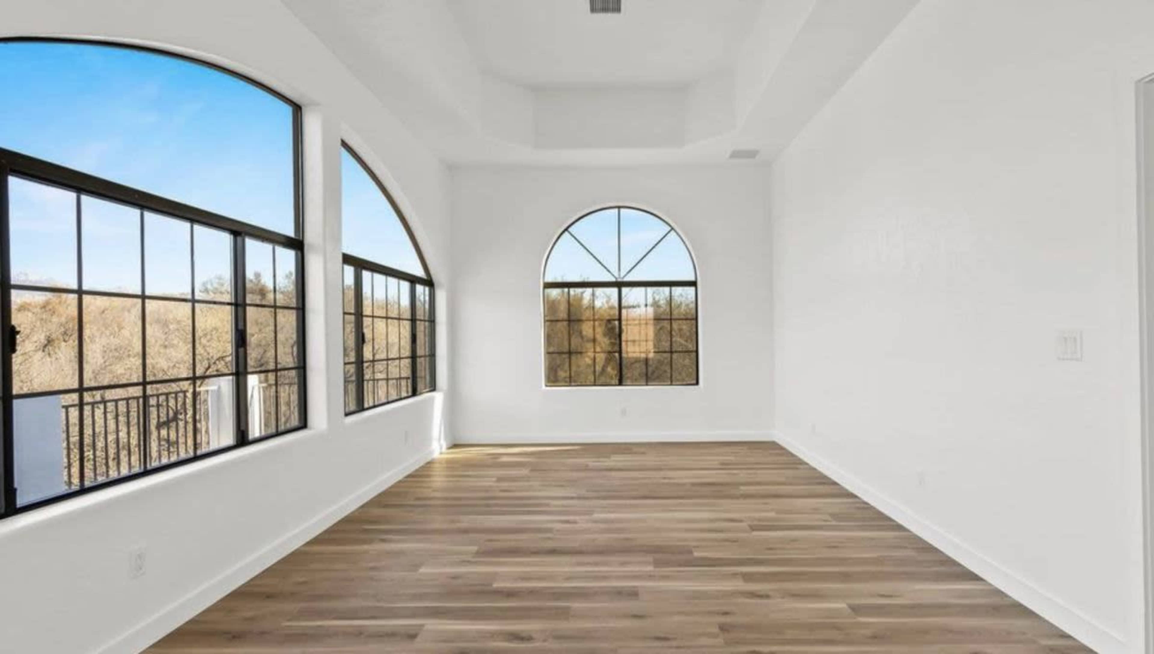 The image shows a spacious, empty room featuring large arched windows that allow natural light to fill the space.