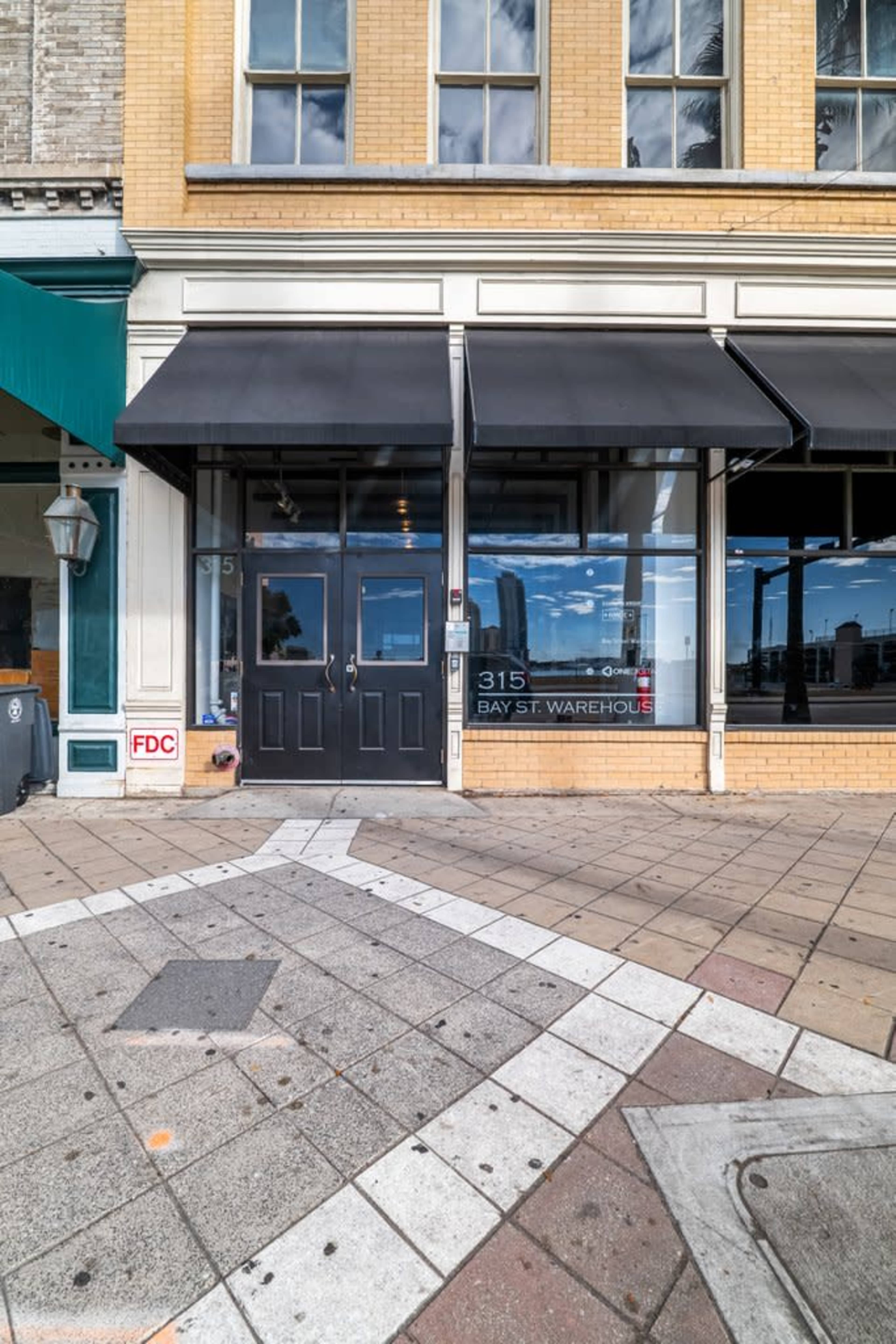 The image shows a storefront of a building with large windows and a double door entrance, featuring an awning, and the sign "315 BAY ST WAREHOUSE."