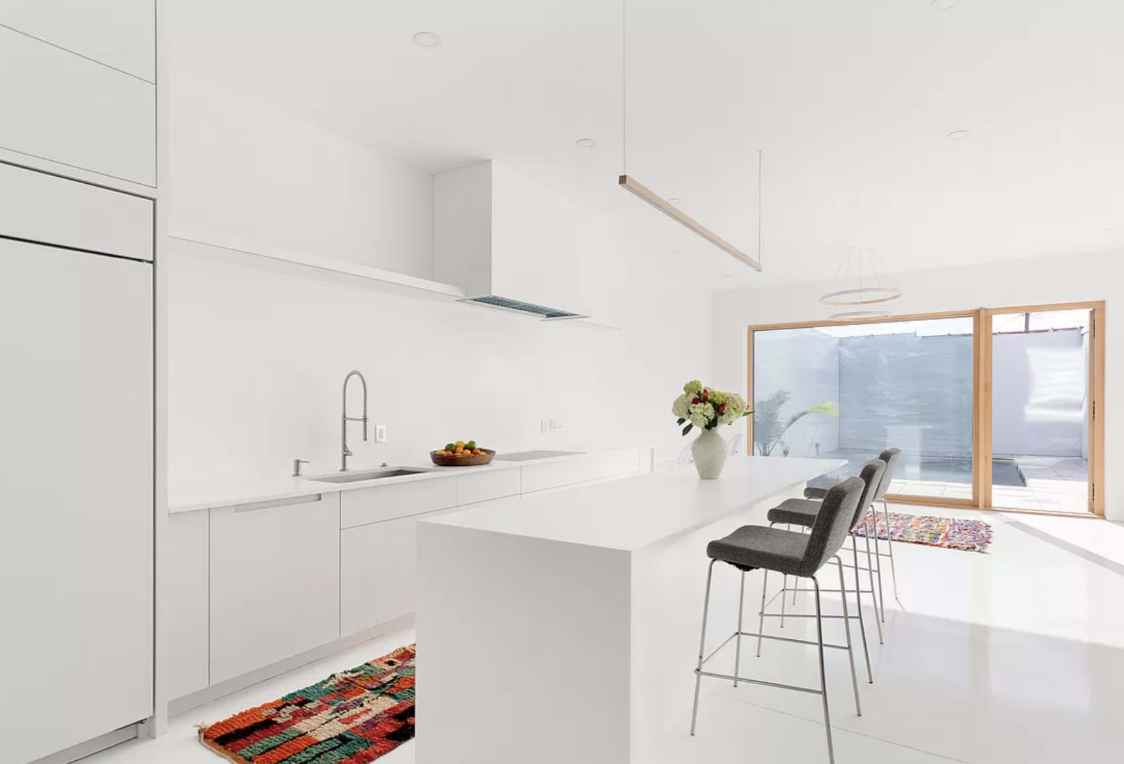 A modern kitchen with white cabinetry, a long island with bar stools, and a sliding glass door leading to an outdoor patio.