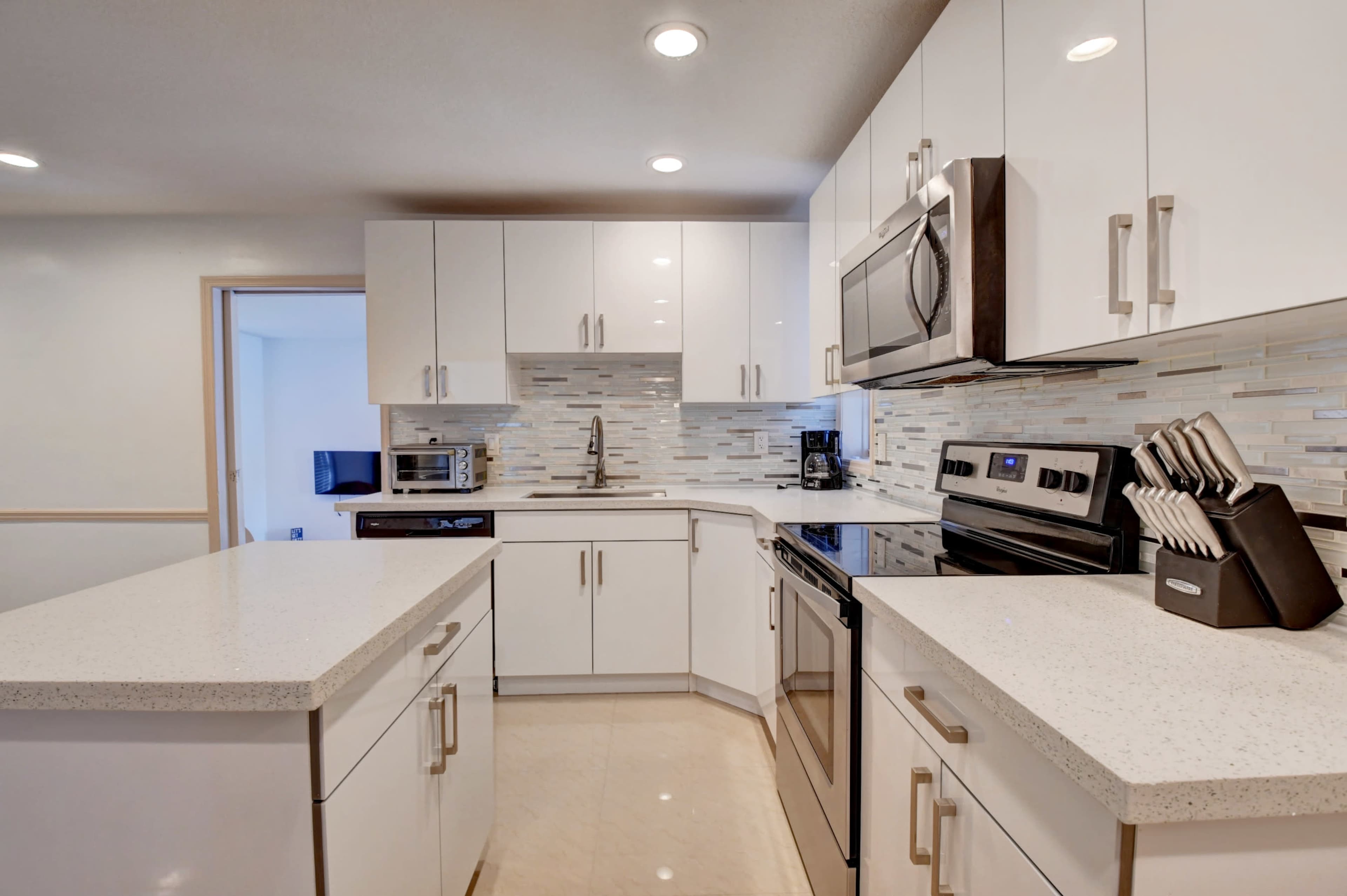 A modern kitchen features white cabinets, stainless steel appliances, and a light-hued countertop with a tiled backsplash.