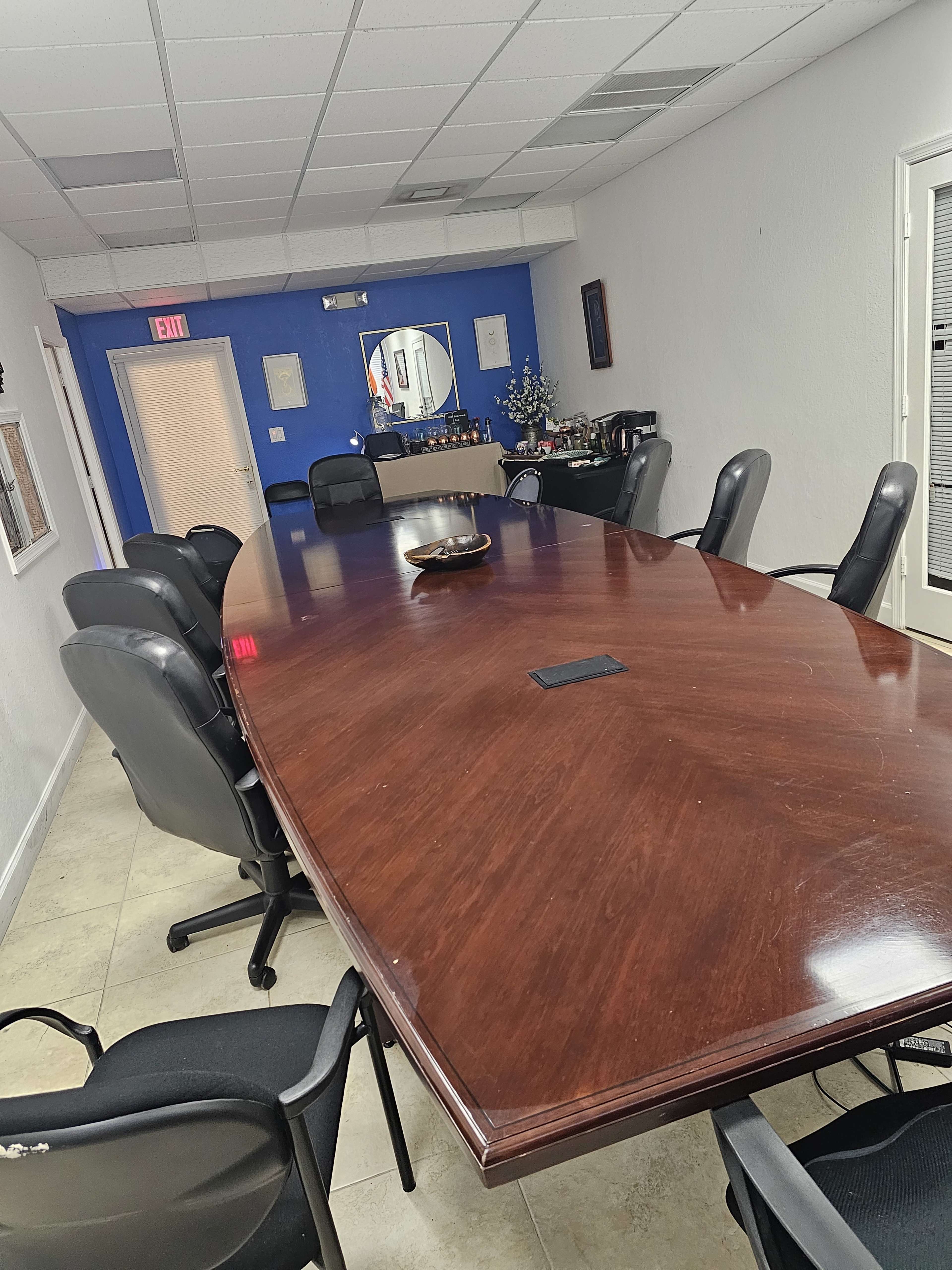 A long wooden conference table surrounded by black chairs in a well-lit meeting room with blue walls.