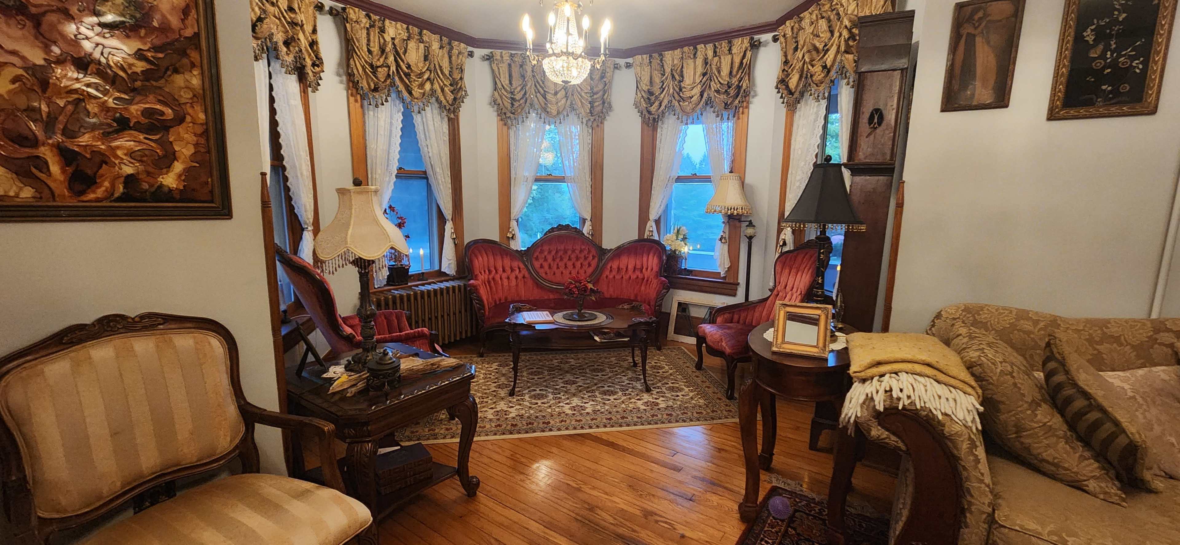 The image shows a Victorian-style living room with ornate furniture, including a pair of red upholstered chairs and a vintage chandelier.