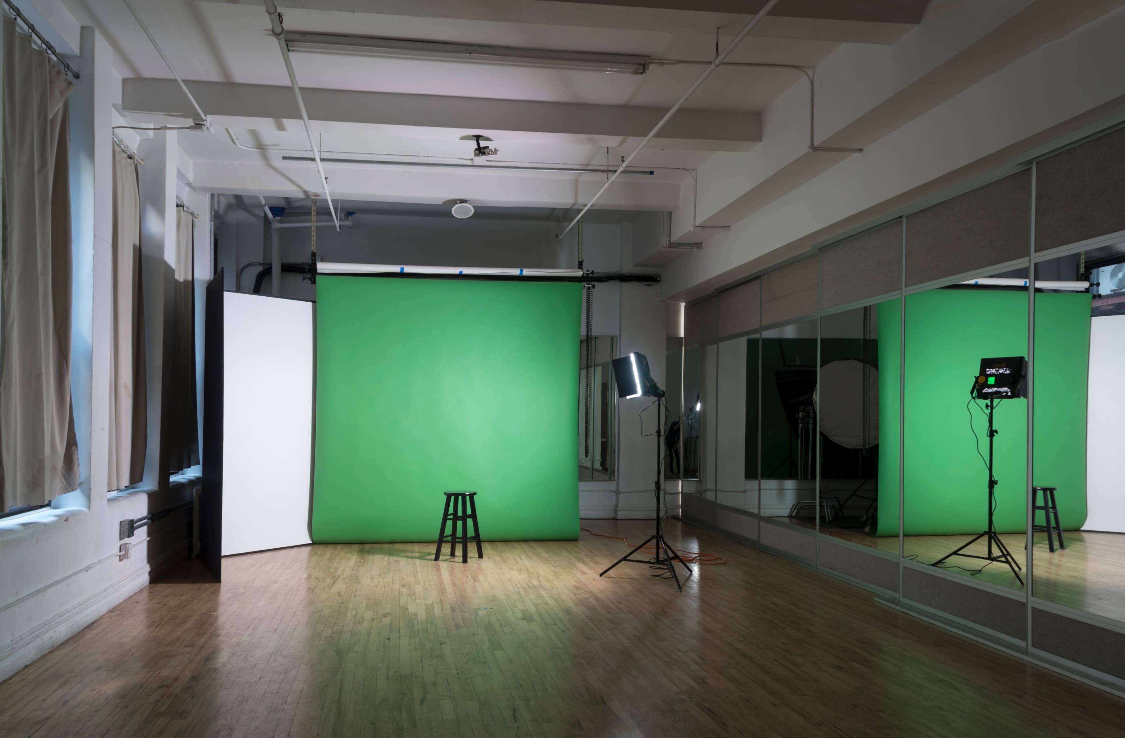 A photography studio features a green backdrop, a wooden stool, lighting equipment, and mirrored walls.