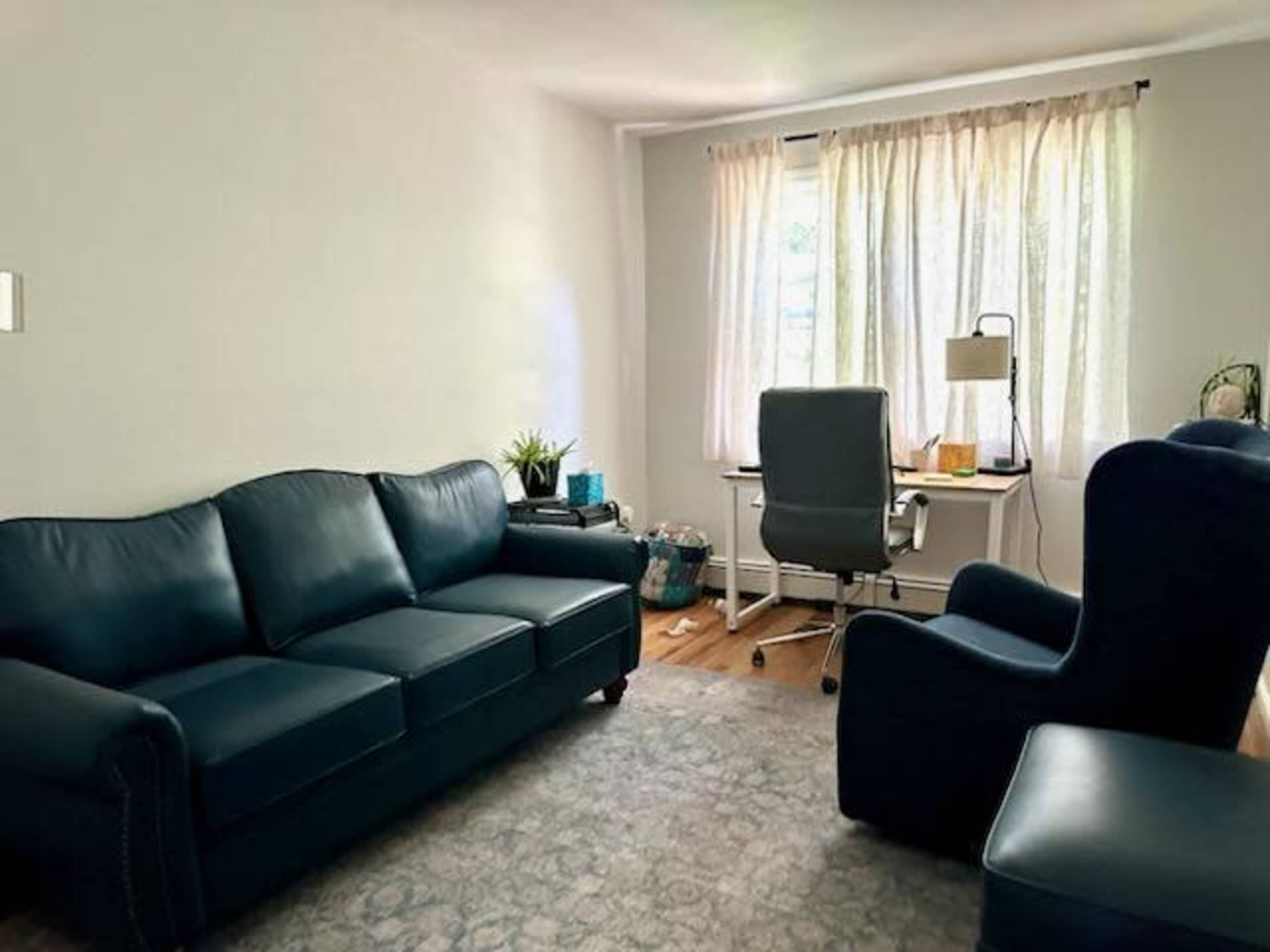 The image shows a living room with a blue couch, an armchair, and a desk with a lamp by a window.