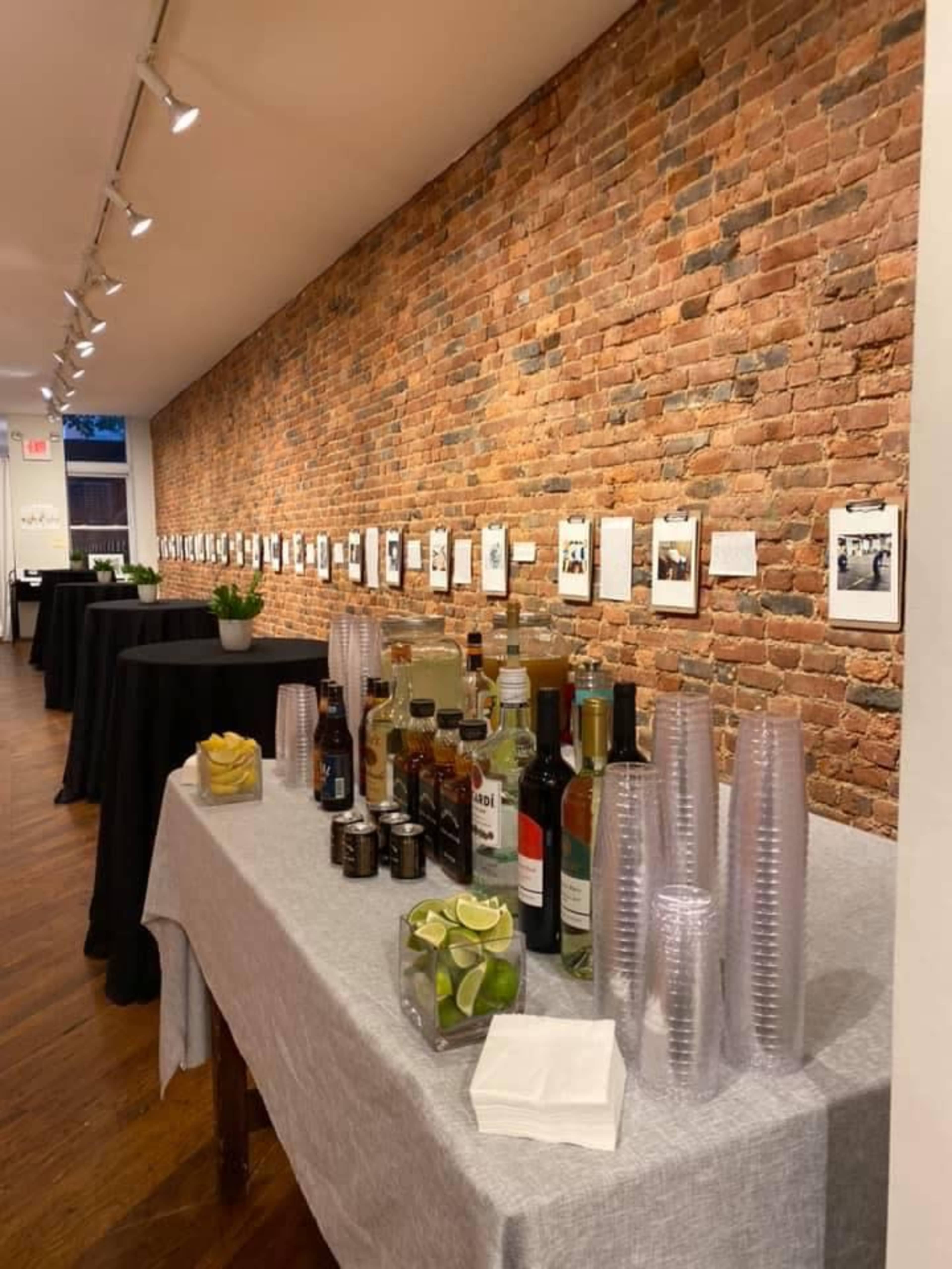 A venue with exposed brick walls contains tables with beverages, glassware, and photo displays on the walls.