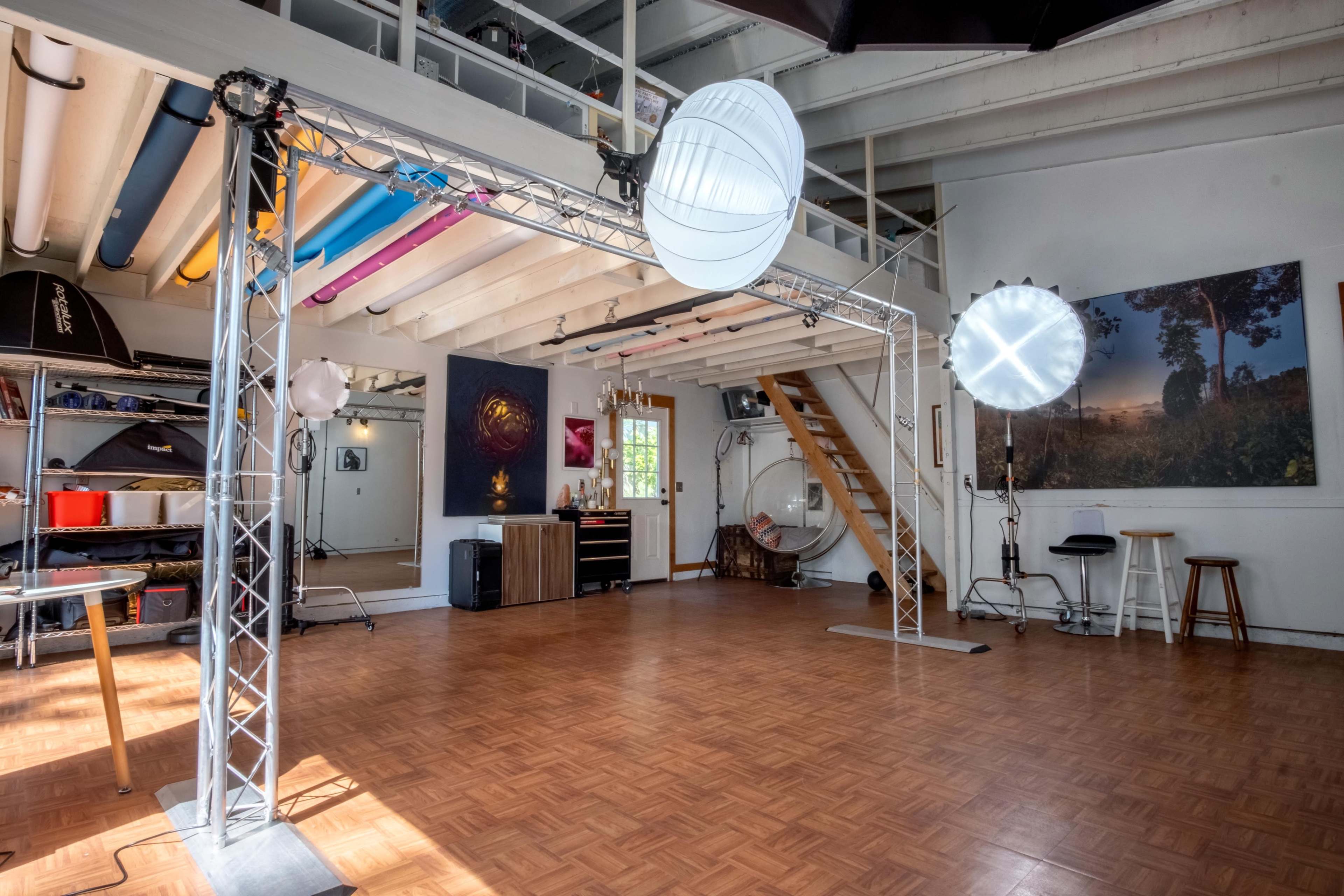 An empty studio space with wooden flooring, soft lighting fixtures, and various equipment along the walls.